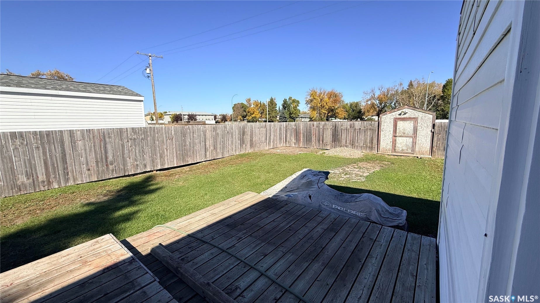 Expansive backyard with a wood deck, wood privacy fencing, a manicured lawn, and an outbuilding