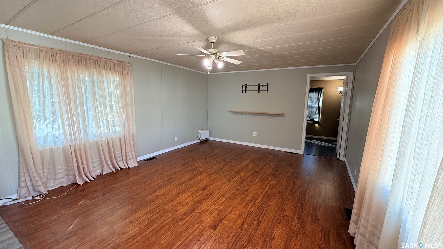 Wood-finish flooring with light-toned wall paneling, featuring a ceiling fan with integrated lighting