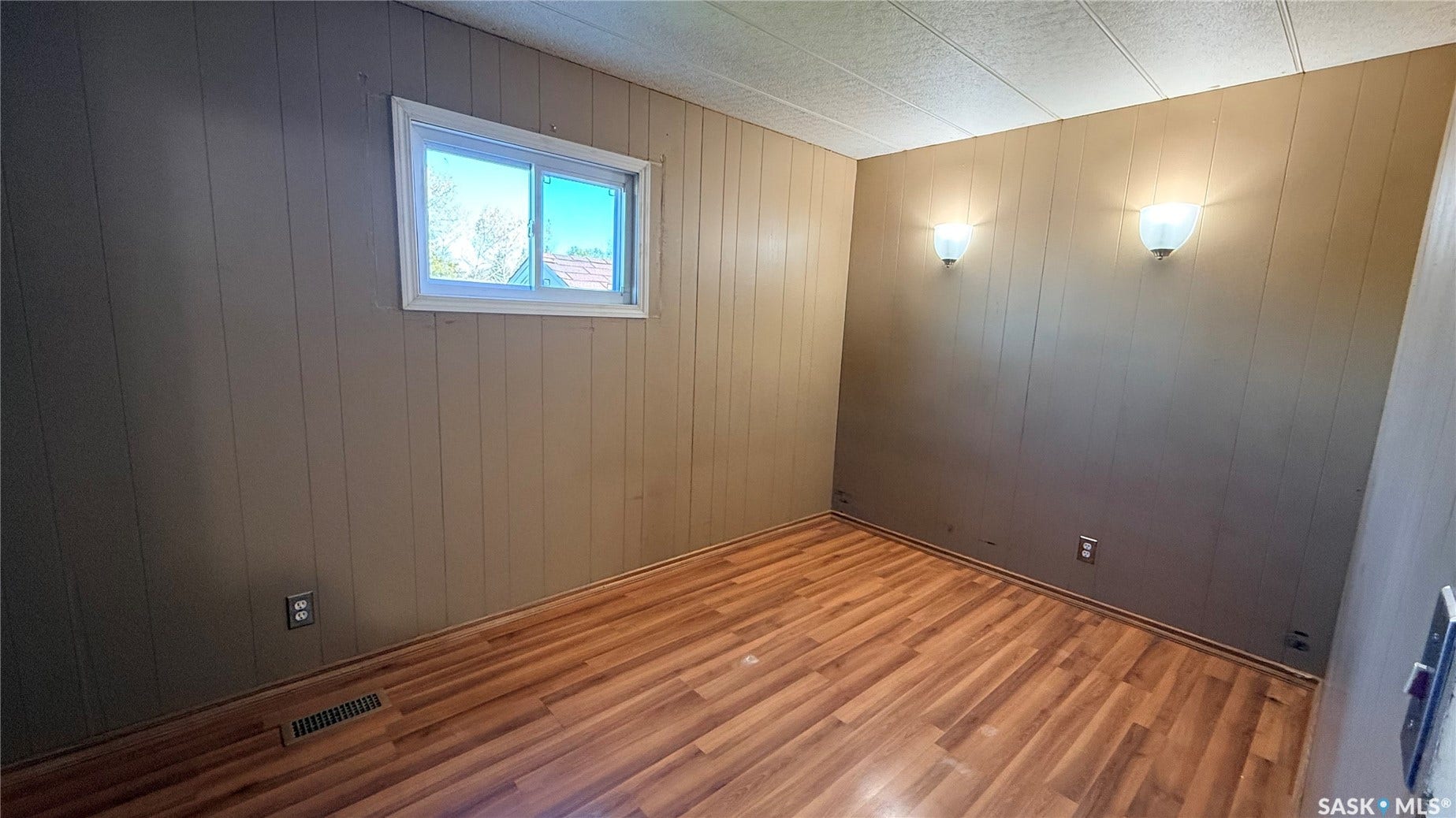 Wood-finish flooring with vertical paneling, a single window, and two wall-mounted light fixtures