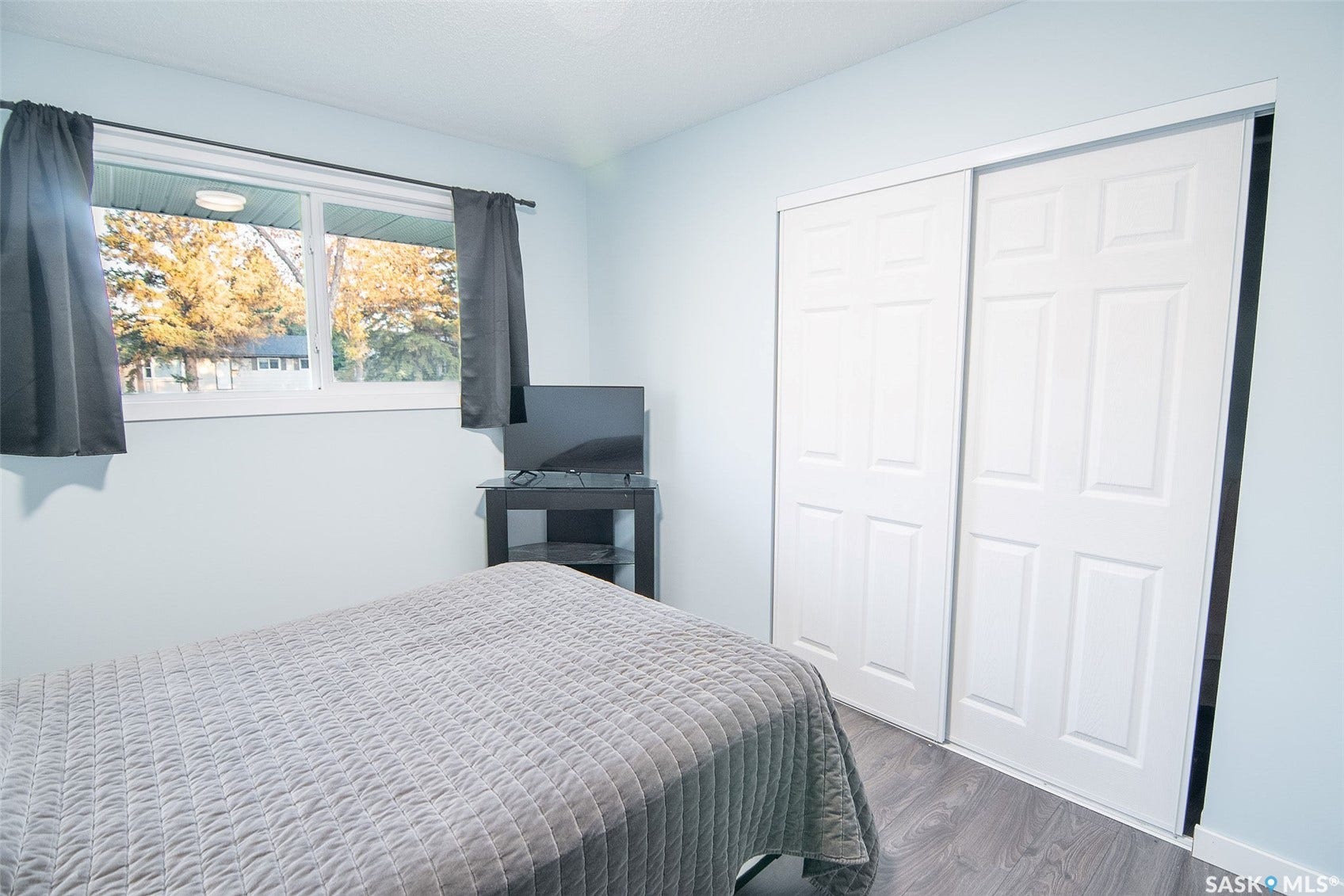Wood-finish flooring, white sliding closet doors, ceiling-mounted light fixture, and a window with exterior scenery