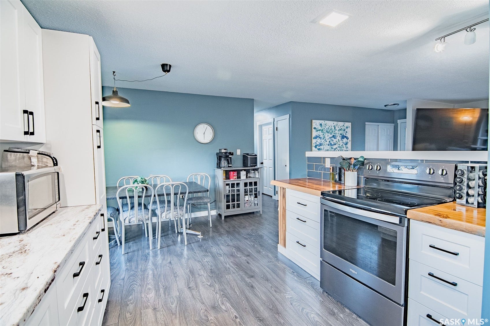 White shaker-style cabinetry with matte black hardware, wood-finish flooring, stainless steel range with cooktop, wood countertops, and a gray subway tile backsplash
