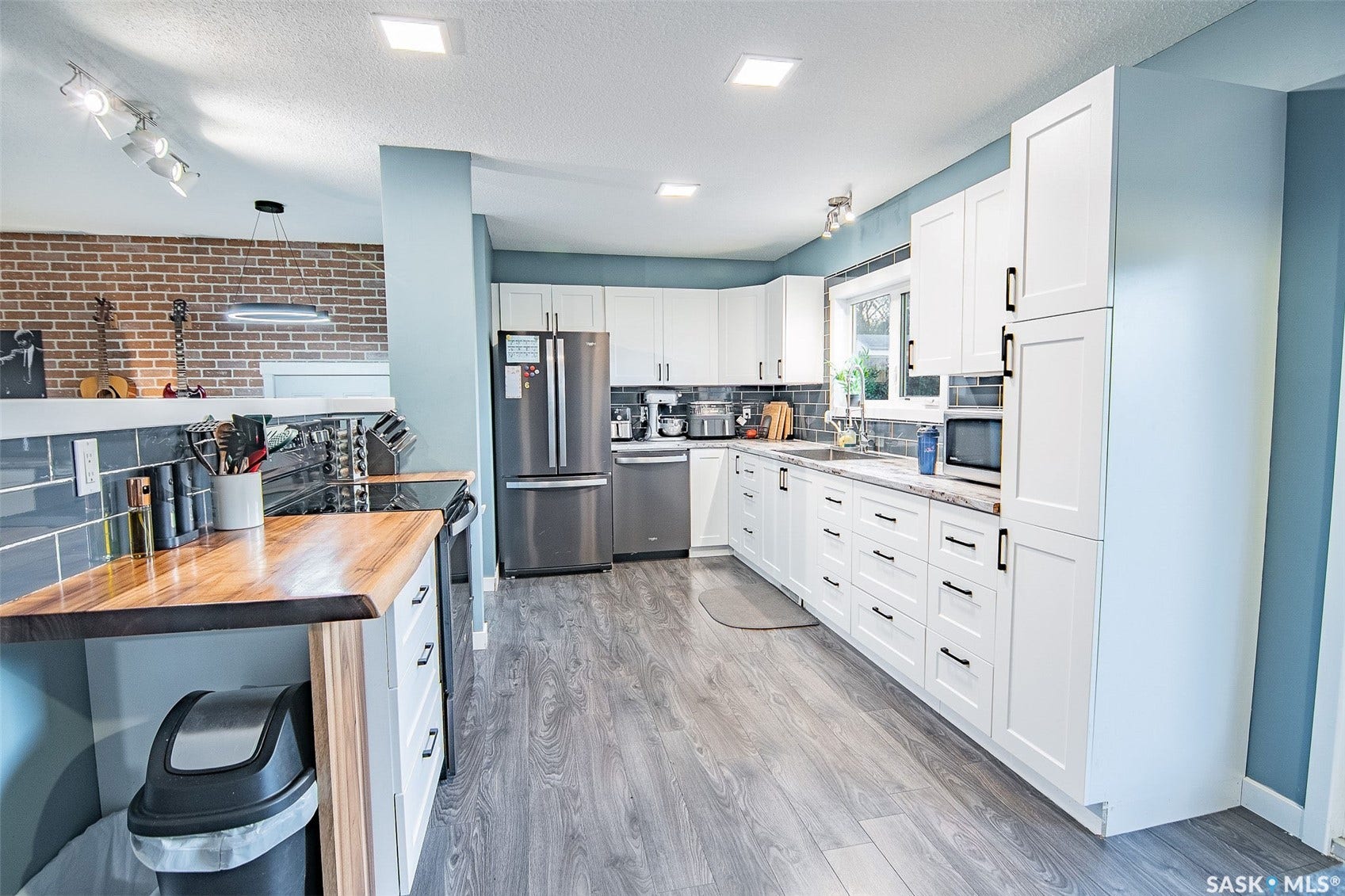 White cabinetry with black hardware, wood-finish flooring, stainless steel appliances, grey subway tile backsplash, and a wood-finish countertop