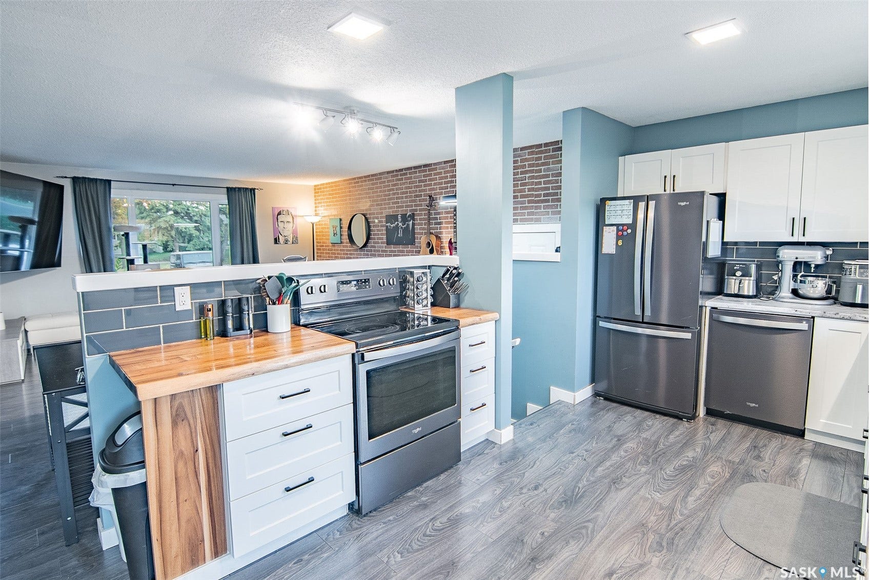 Kitchen featuring wood-finish flooring, white cabinetry with dark pulls, a grey subway tile backsplash, and stainless steel appliances
