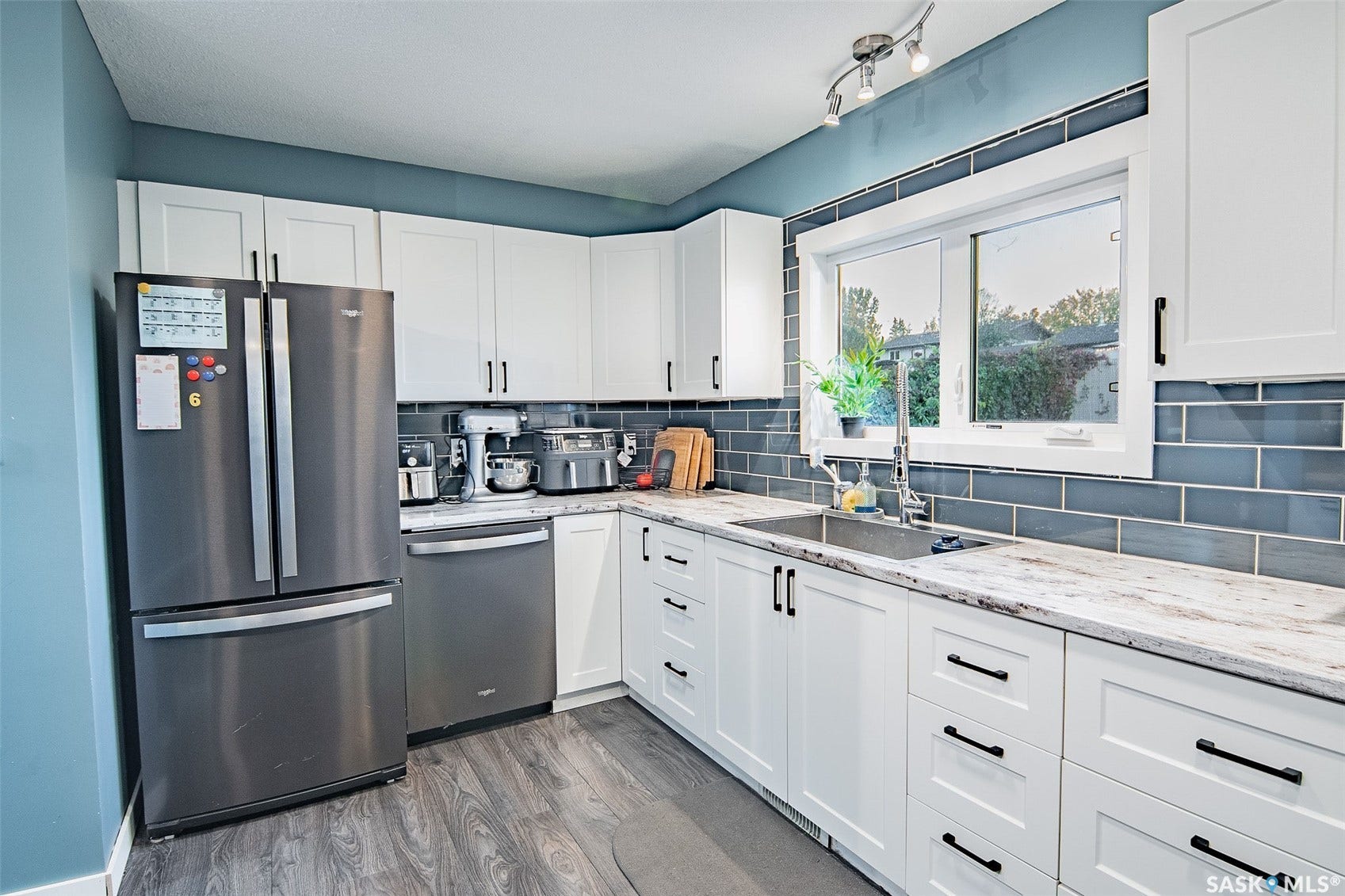 White cabinetry with black hardware, wood-finish flooring, undermount stainless steel sink, large window, and subway tile backsplash