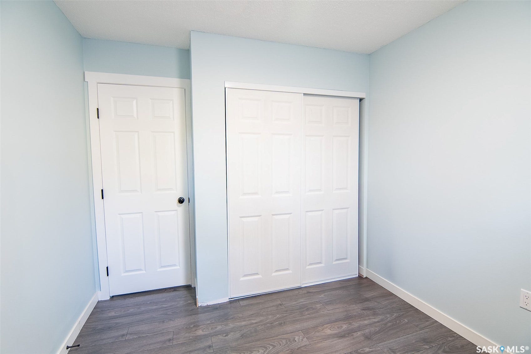 Wood-finish flooring, white bi-fold closet doors, white six-panel door, white trim, and light blue wall finish