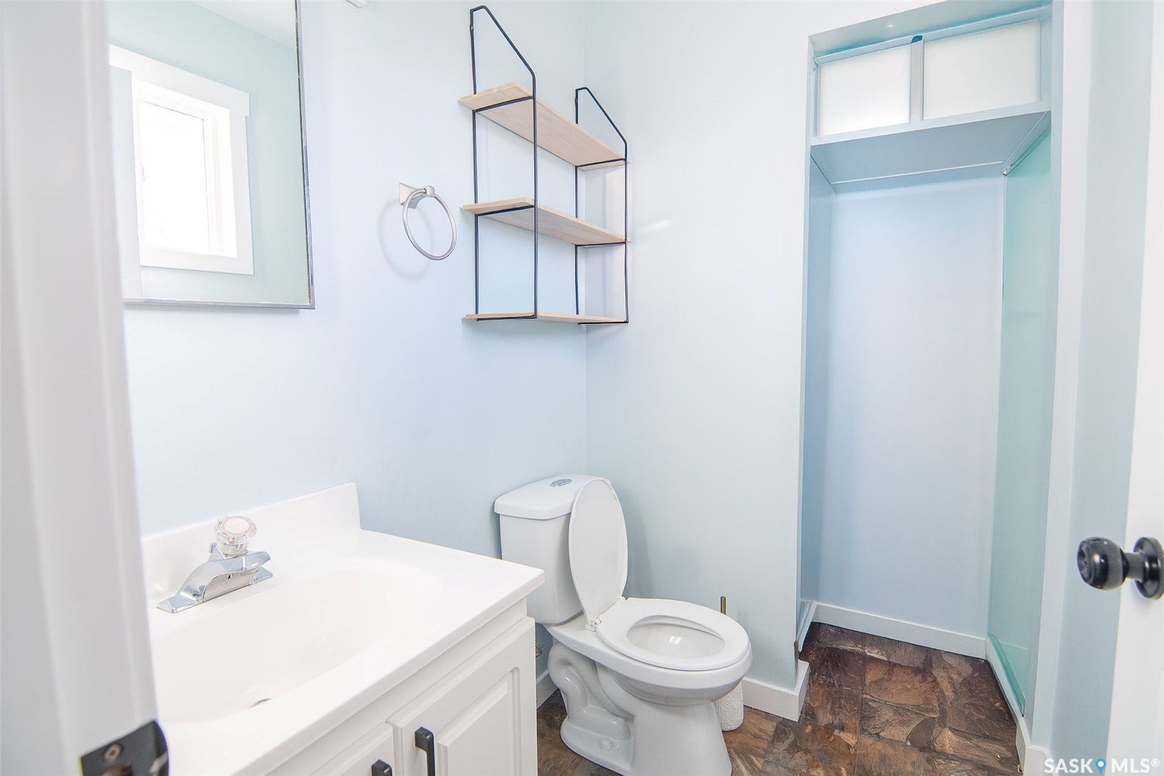 Integrated vanity with a white countertop and sink, wall-mounted mirror, modern shelving unit, and a built-in shower enclosure