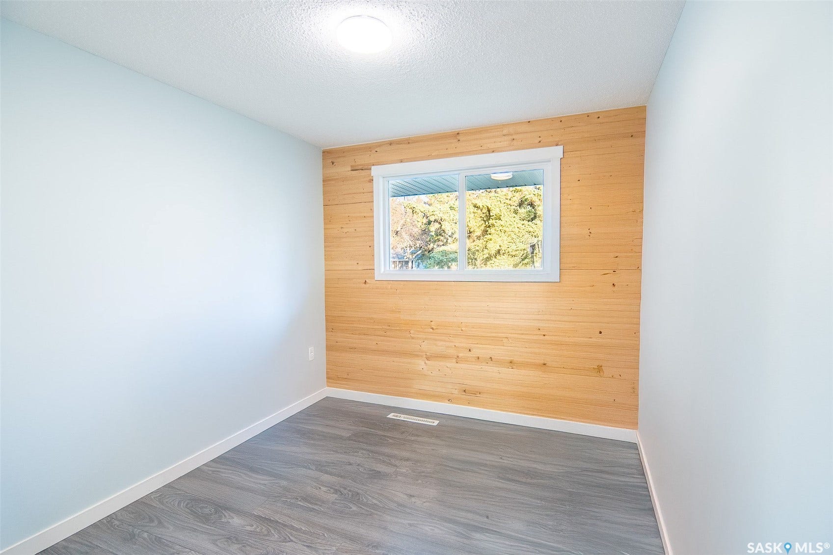 Light-toned wood panel accent wall with a window, contemporary ceiling light fixture, light gray walls, and wood-finish flooring