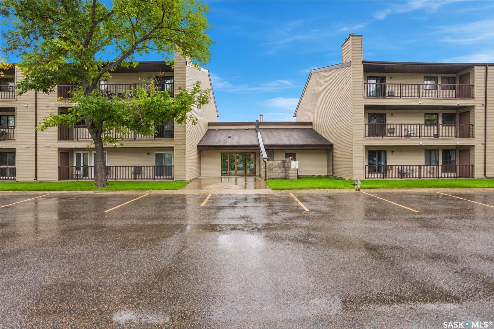 Multi-level complex with private balconies, a central entrance, and ample paved parking