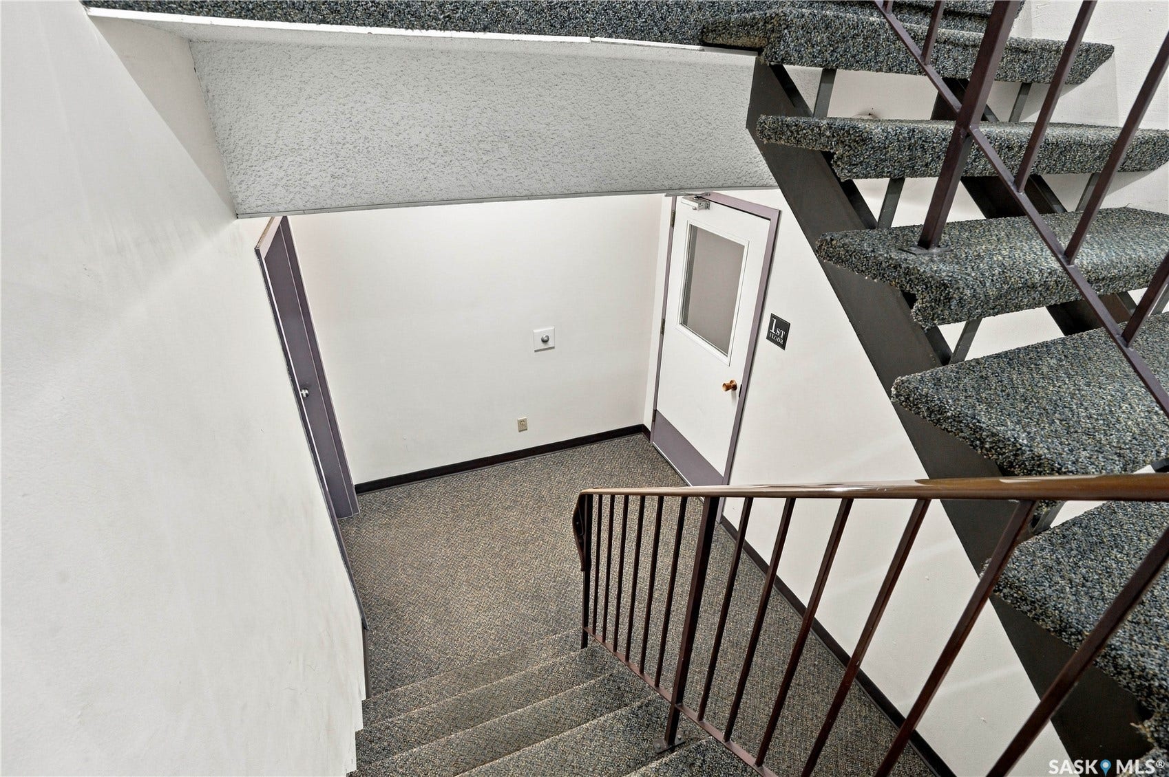 Carpeted stairwell with metal handrails, leading to a landing with a white door featuring a frosted glass panel