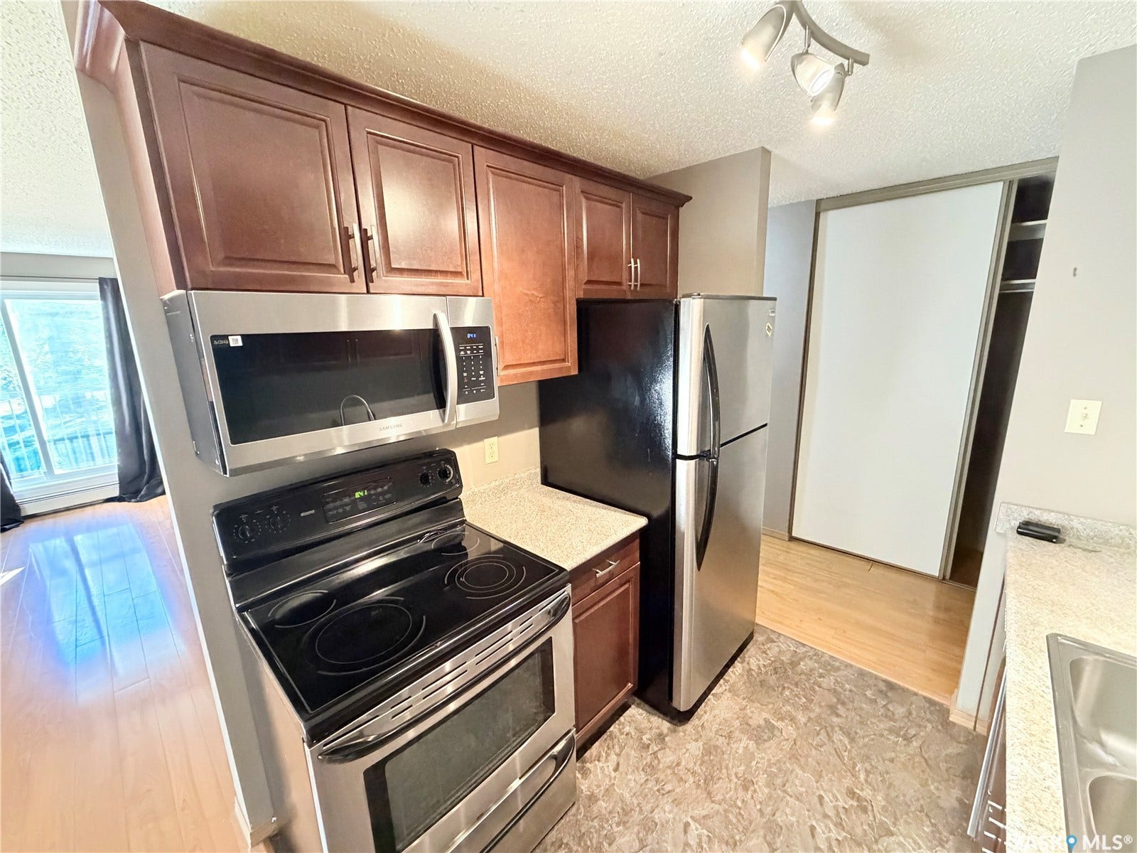 Kitchen featuring stainless steel appliances, wood cabinetry, stone-finish countertops, and track lighting