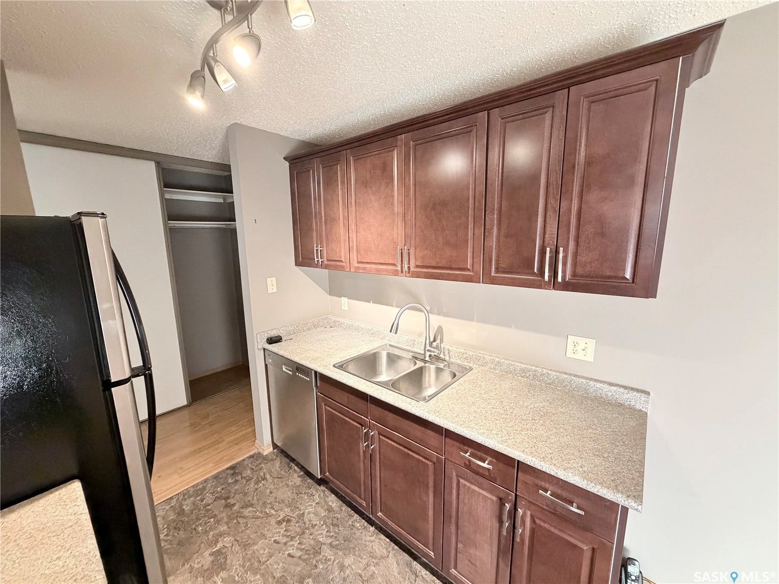 Kitchen featuring wood-finish cabinetry, stainless steel double-basin sink, light-toned countertops, and track lighting