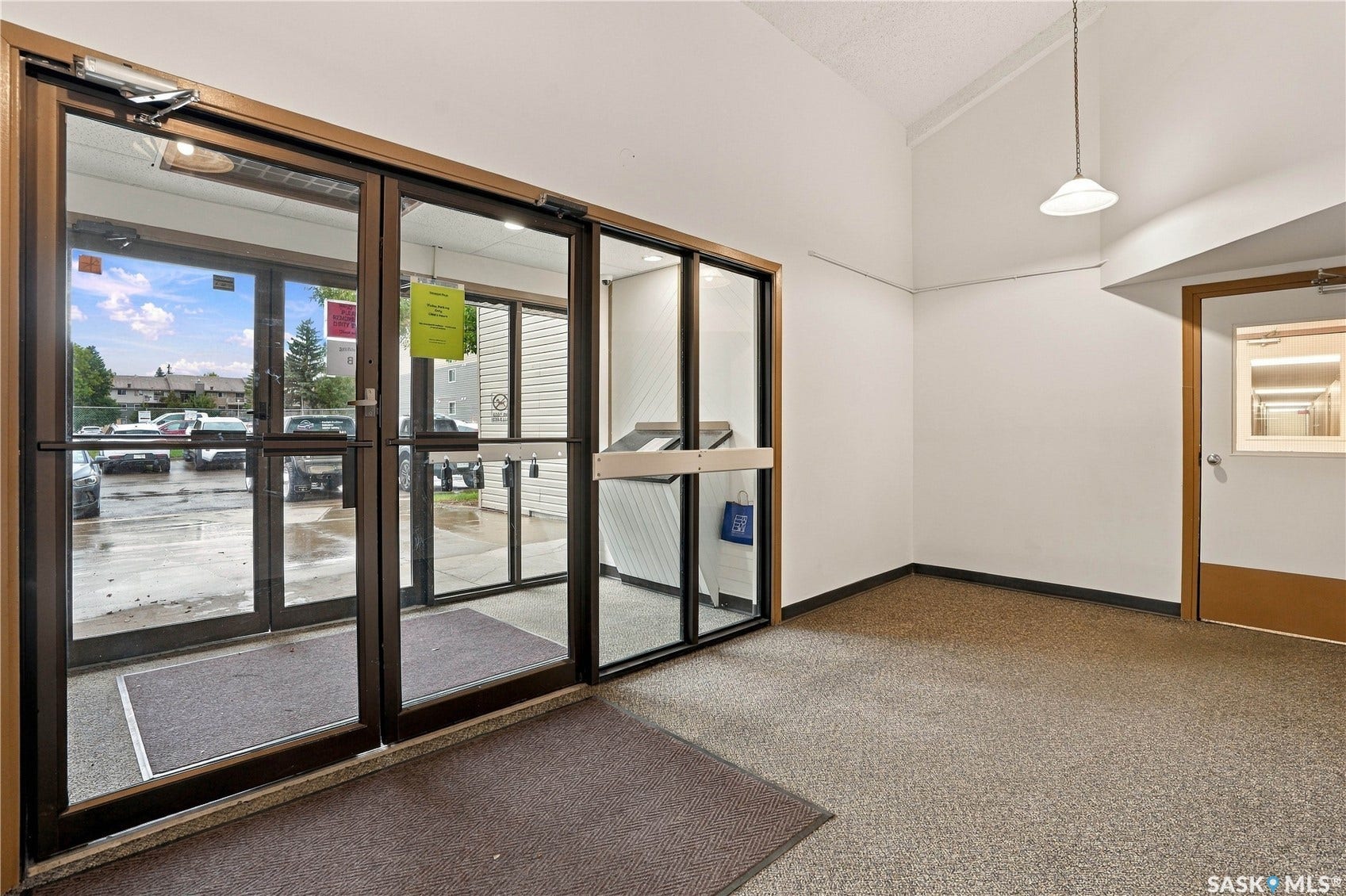Entryway featuring double glass doors, a single pendant light fixture, and textured carpeting
