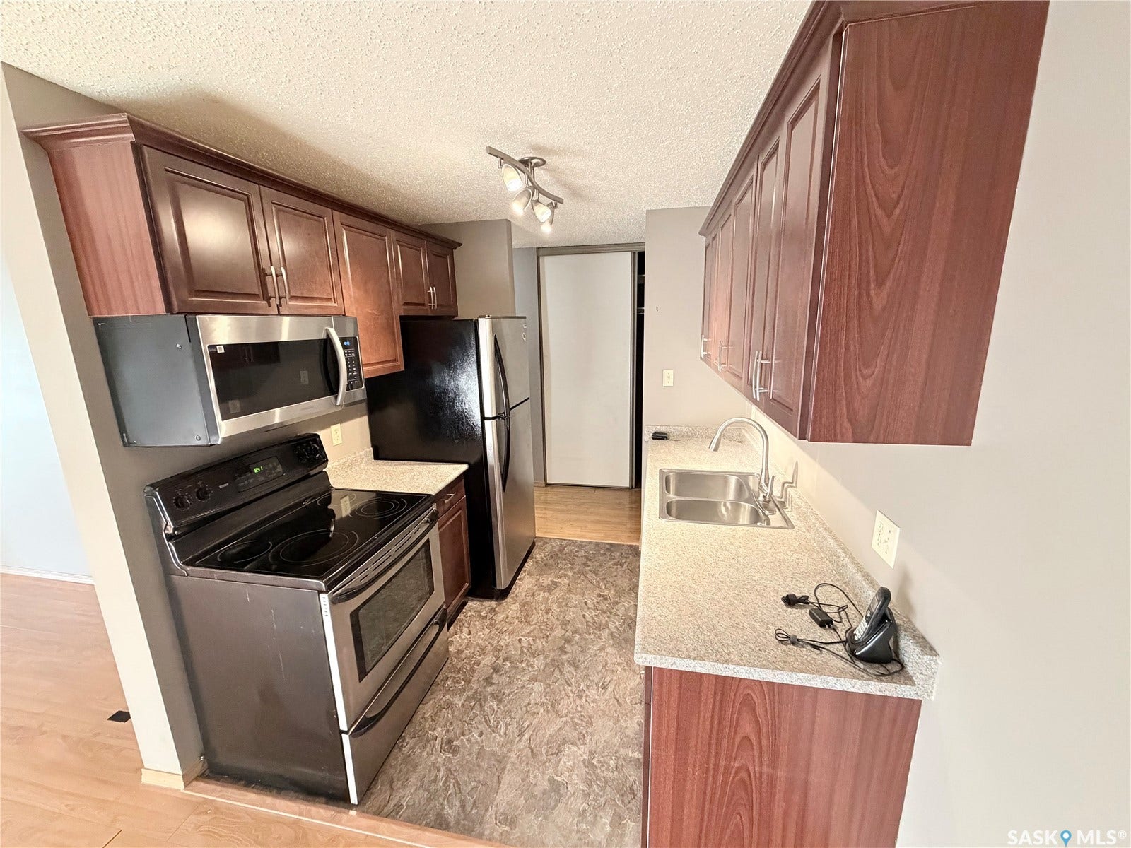 Kitchen featuring wood-finish cabinetry, stainless steel appliances, speckled countertops, and a double basin sink