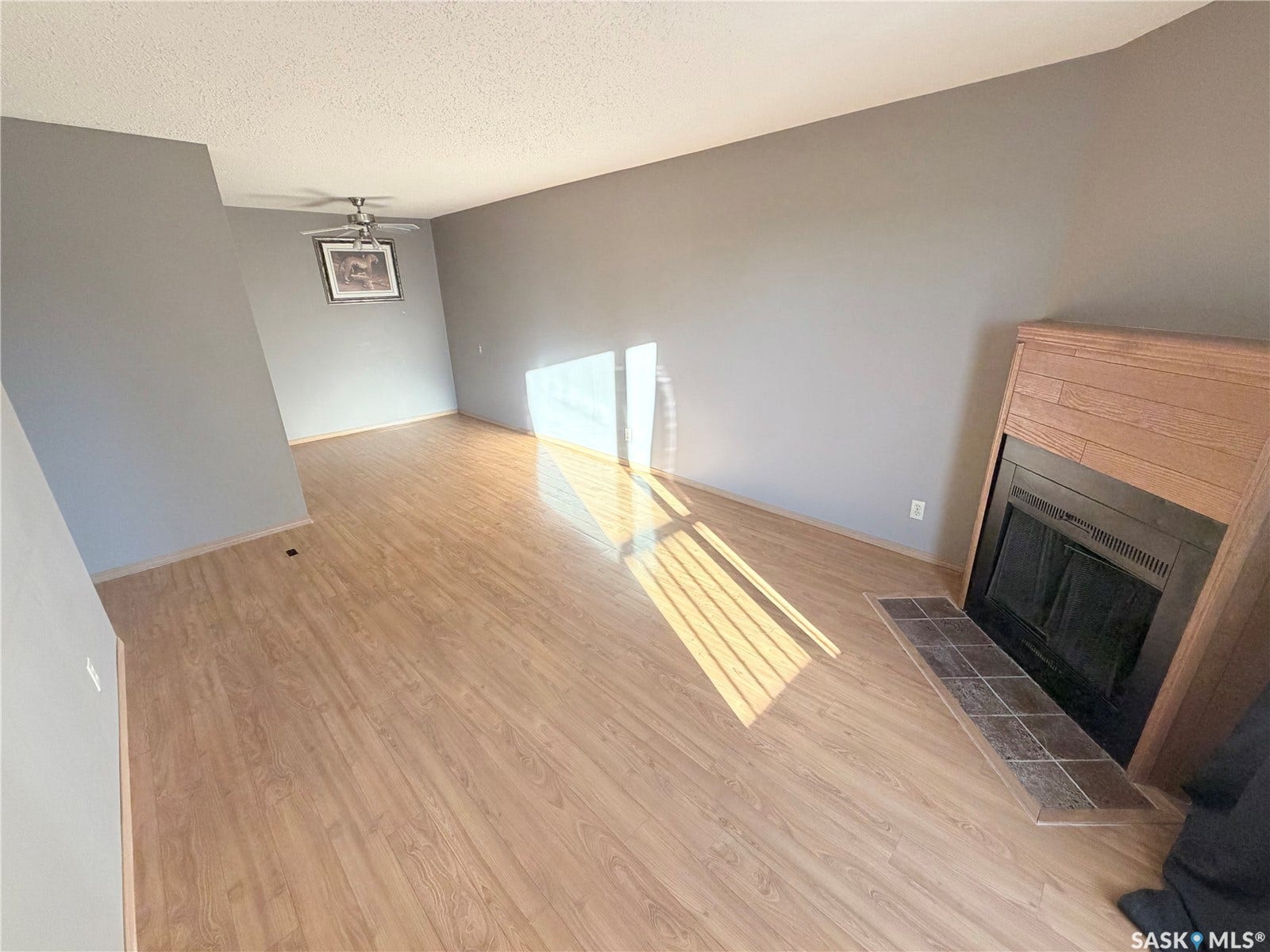 Spacious room featuring wood-finish flooring, a ceiling fan, and a fireplace with a wood mantle and tile hearth