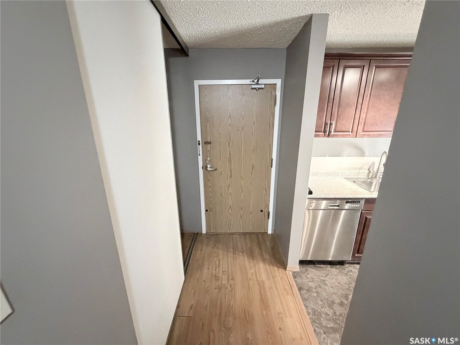 Wood-finish flooring, light tone cabinetry, stainless steel dishwasher, undermount sink, and light-toned countertop