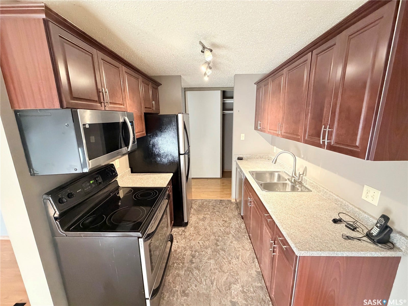 Galley kitchen featuring wood-finish cabinetry, stainless steel sink, over-the-range microwave, and matching countertop