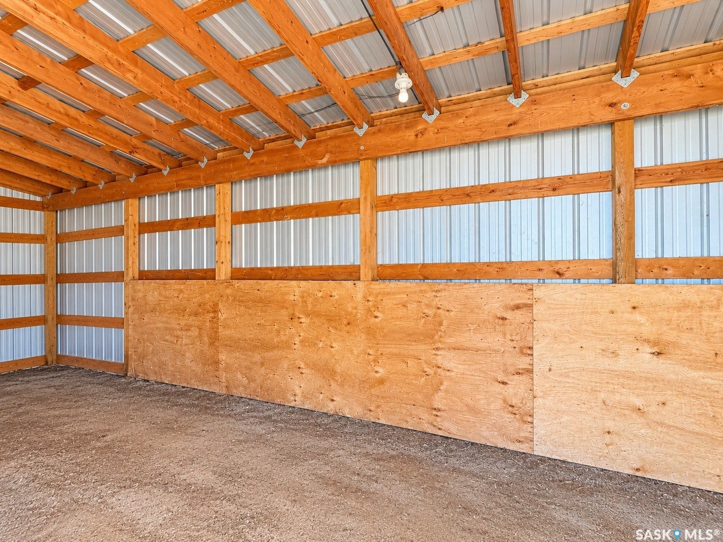 Exposed wood beam construction, corrugated metal roofing, plywood wall surfacing, and a gravel base
