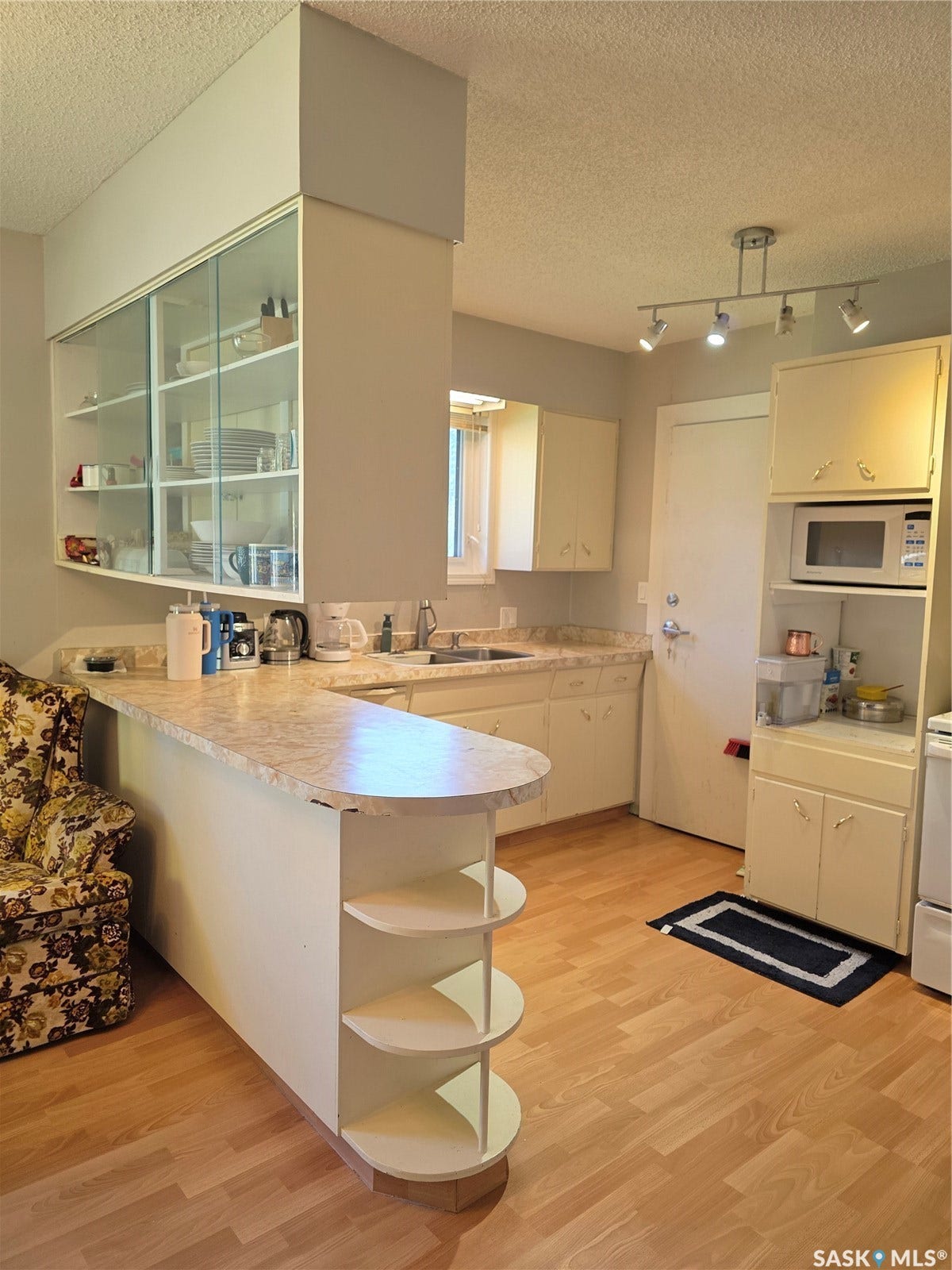 Laminate wood-finish flooring, track lighting, built-in shelving, and upper cabinetry with glass-front doors