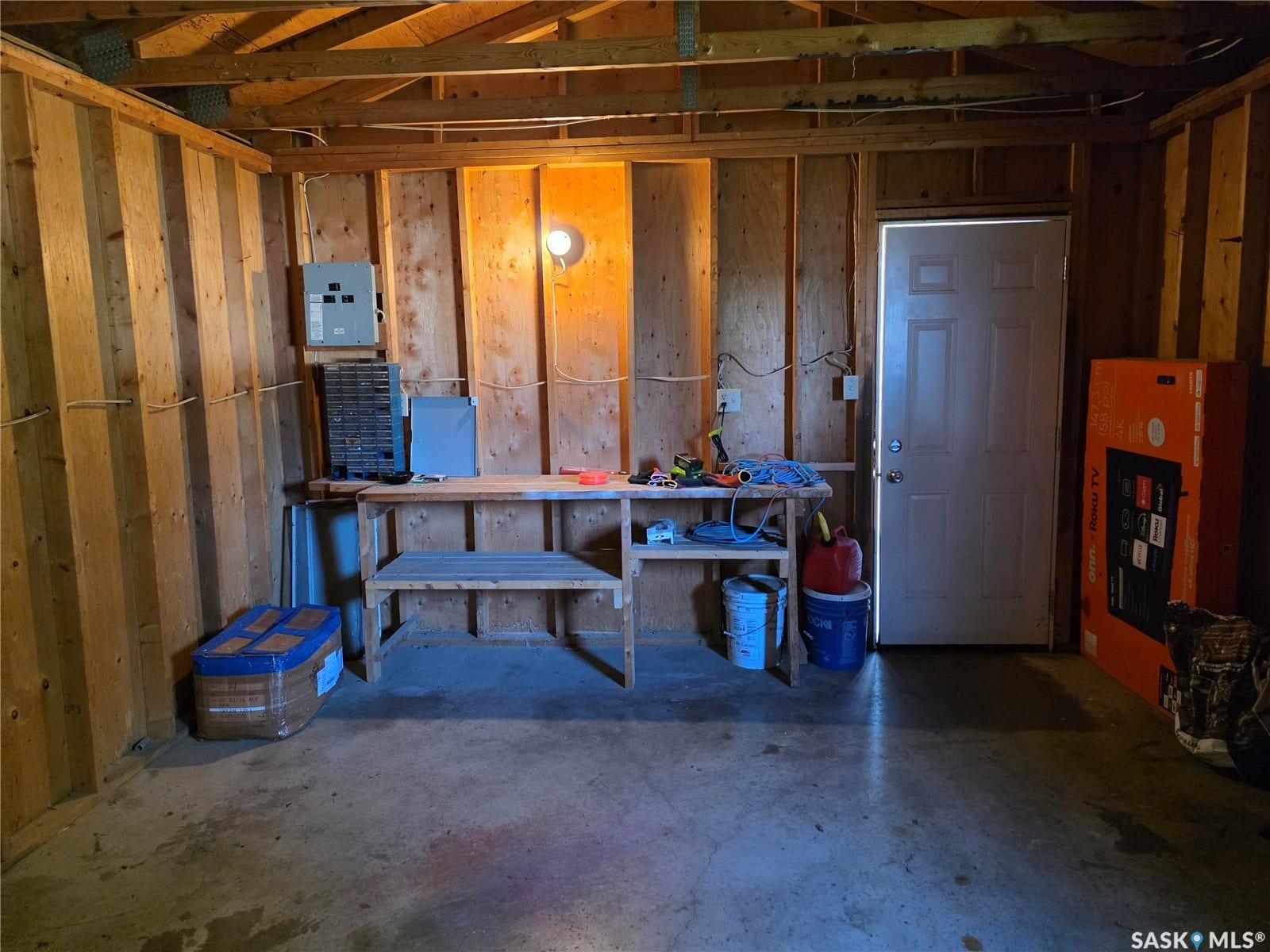Interior wood-paneled walls, exposed ceiling joists, concrete flooring, built-in workbench, and wall-mounted electrical panel