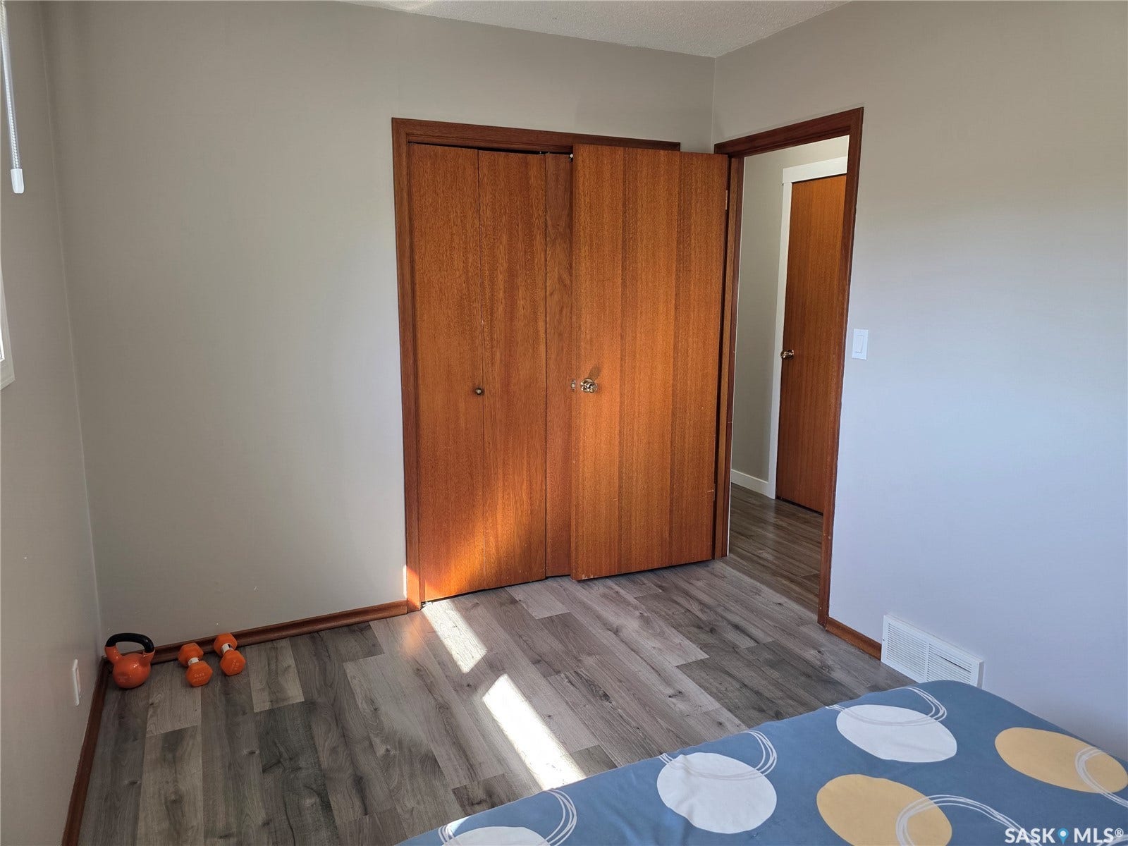 Spacious bedroom featuring wood-finish flooring, double wood-panel closet doors with hardware, and bright natural light from multiple windows