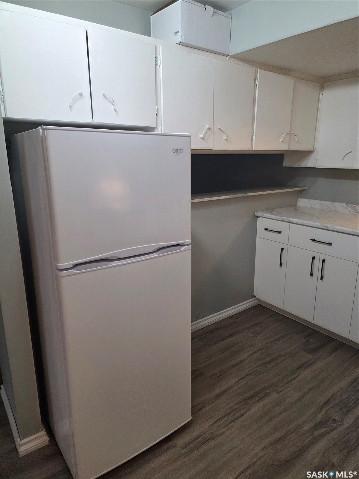 White upper and lower cabinetry, wood-finish flooring, a white refrigerator, and a light-colored countertop