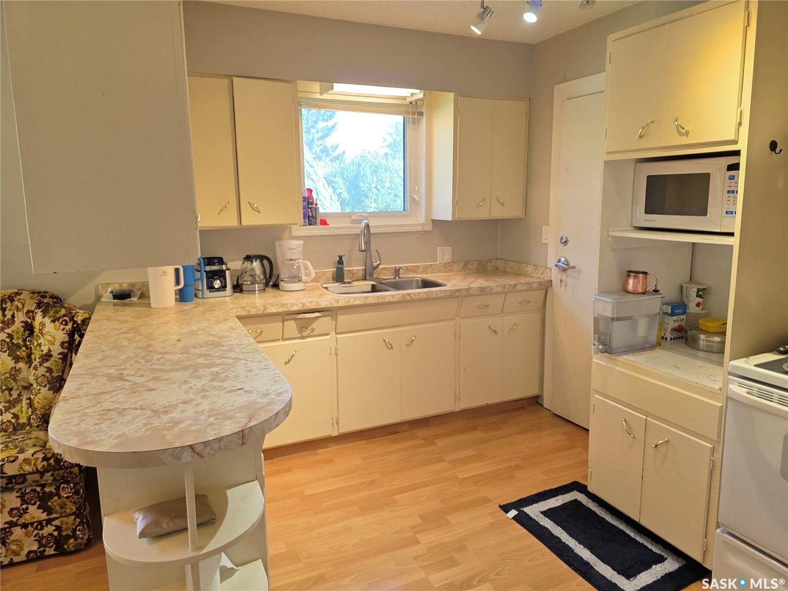 Kitchen featuring light wood-finish flooring, cream cabinetry, a built-in microwave shelf, a stainless steel sink, and track lighting