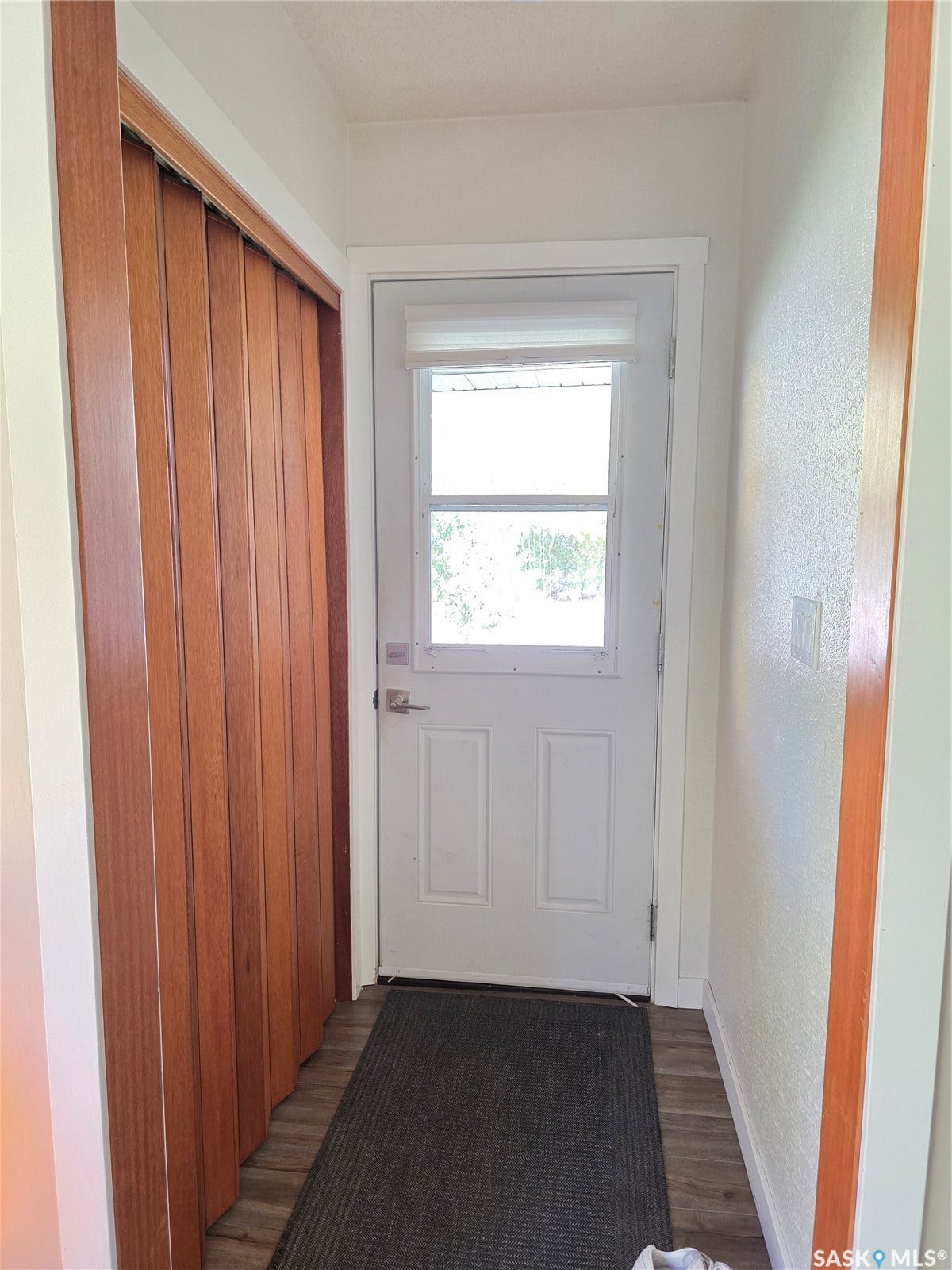 White entry door with upper window, wood-finish flooring, and wood-toned accordion closet doors