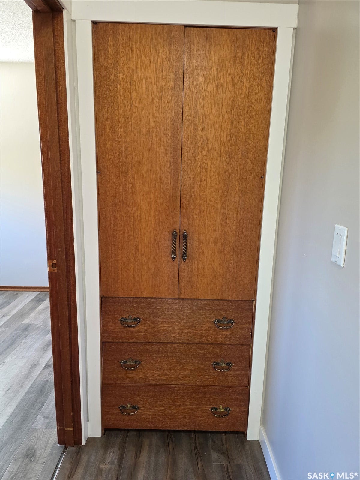 Built-in wood-finish cabinetry featuring upper storage and three lower drawers with brass hardware