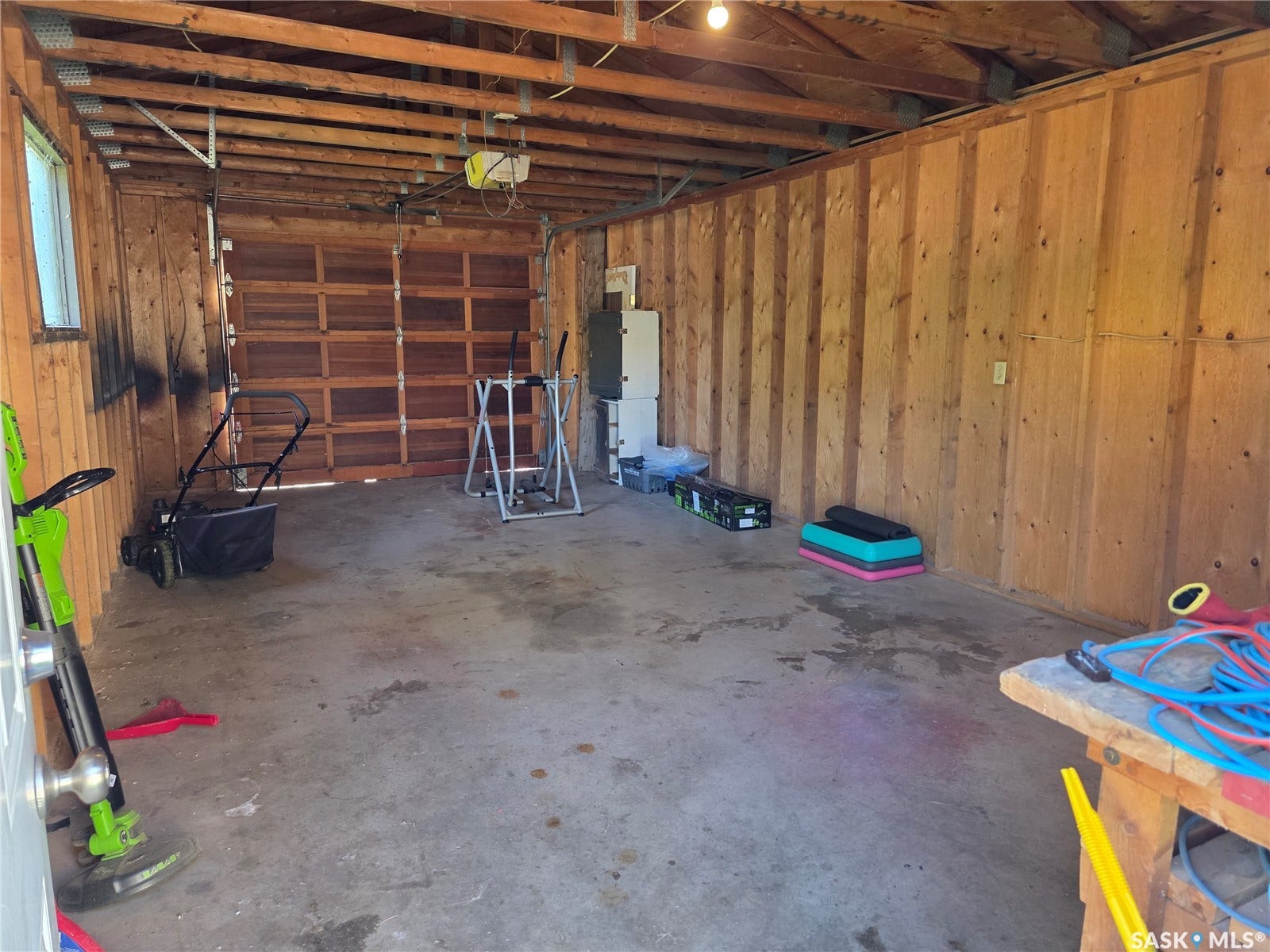 Garage space featuring a concrete floor, exposed wood beam ceiling, wood plank walls, and a window