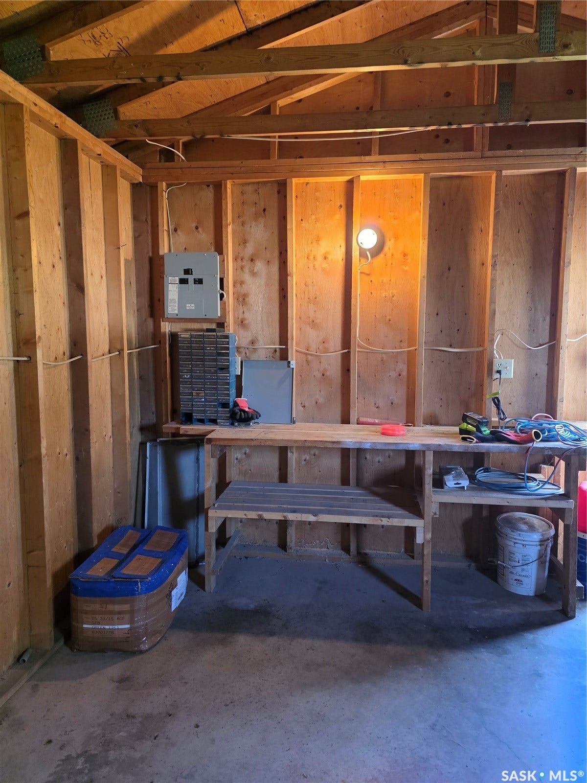 Exposed wood beam ceiling, unfinished wood wall construction, concrete flooring, built-in wooden workbench, and overhead lighting