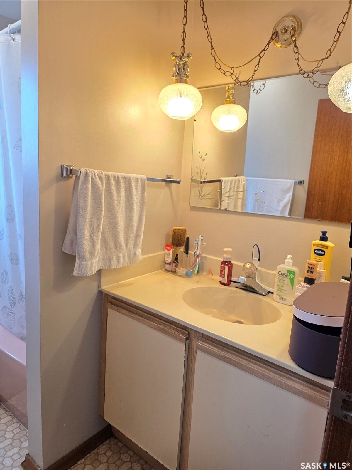 Vanity with light-colored countertop and integrated sink, dual-door base cabinetry, and overhead mirror with decorative lighting