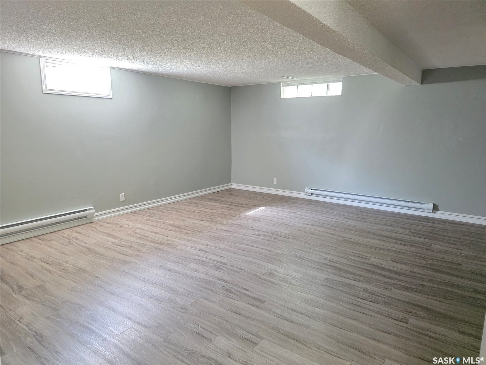 Spacious room featuring light gray walls, wood-finish flooring, and white trim