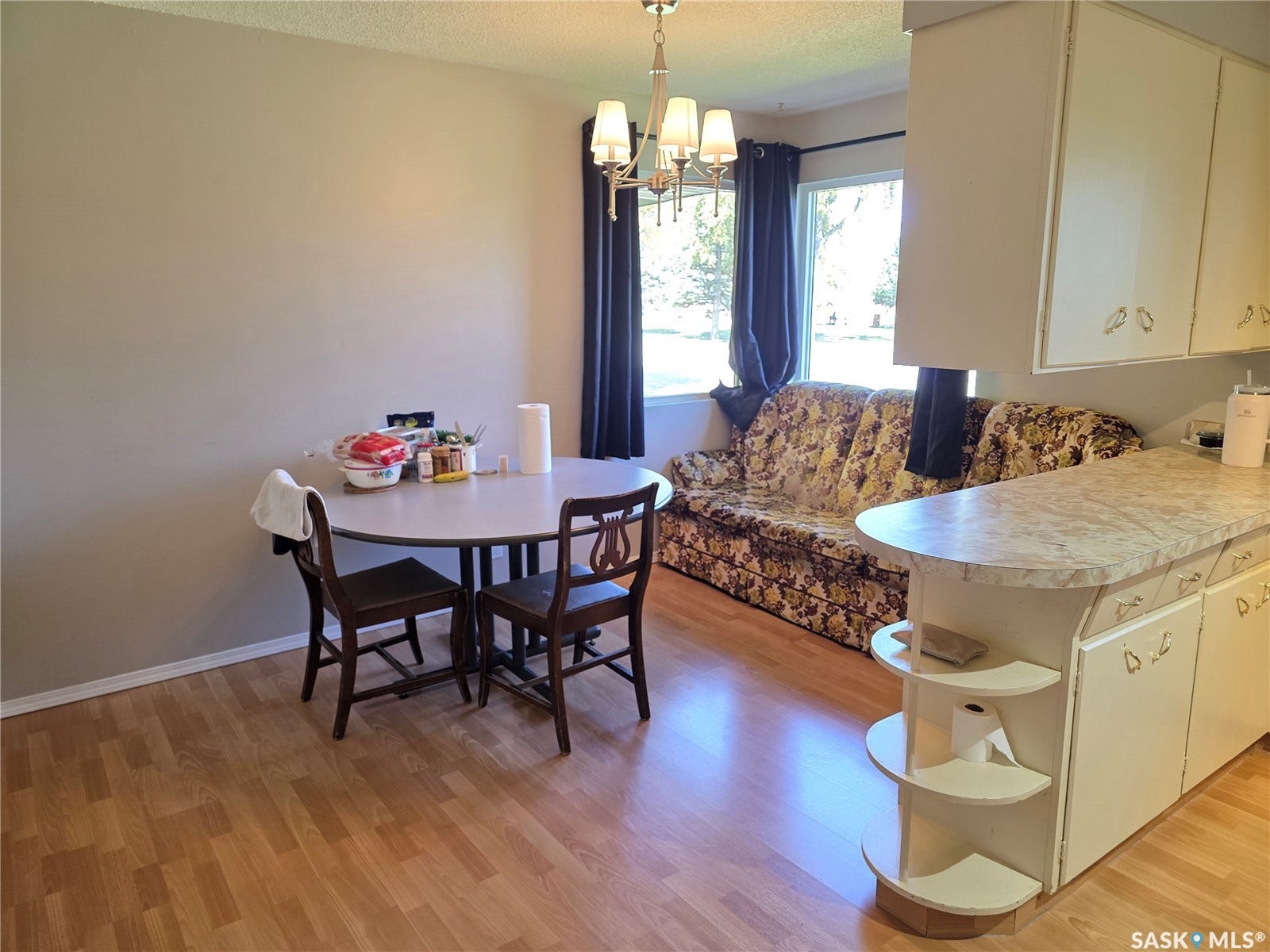 Wood-finish flooring, overhead chandelier, window with opaque drapes, built-in shelving, and white cabinetry with decorative pulls