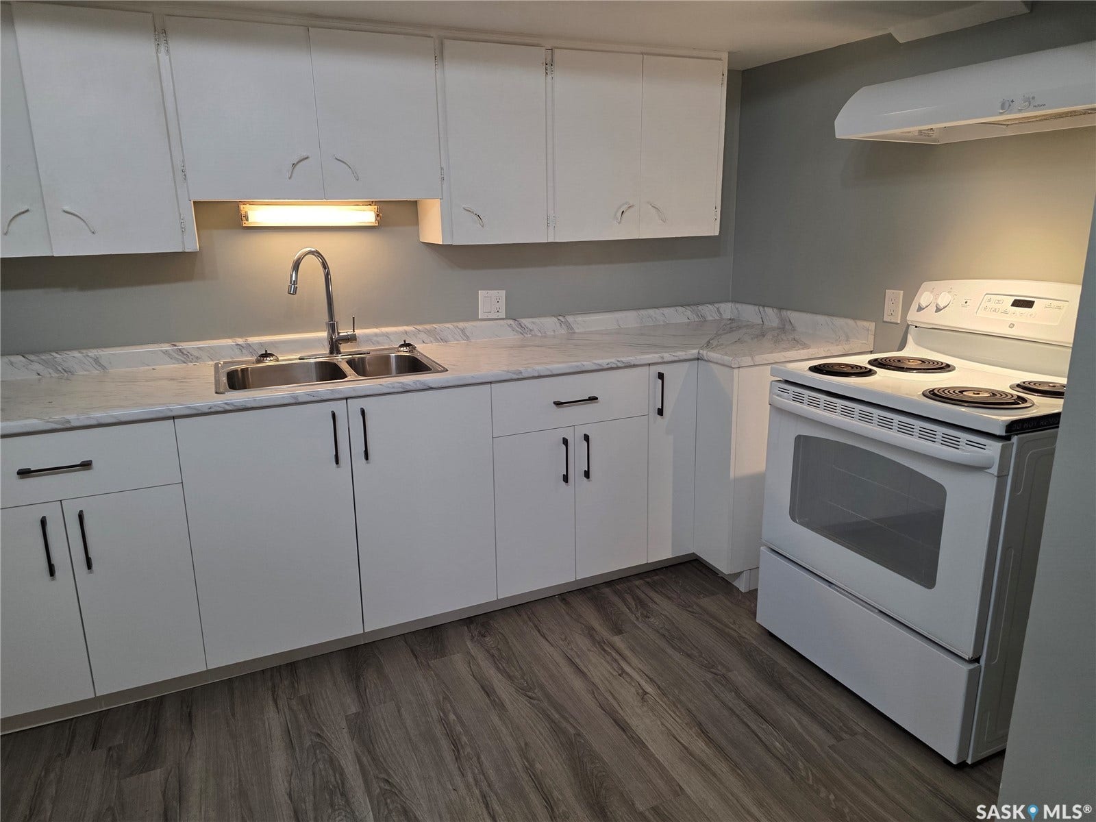 White cabinetry with black hardware, stainless steel double basin sink, white range, wood-finish flooring, and light-toned countertops