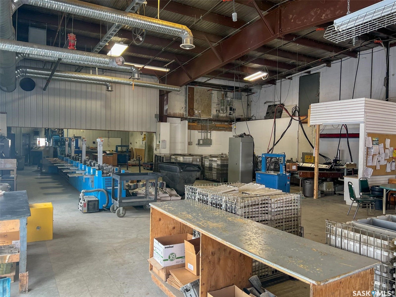 Industrial interior featuring exposed ductwork, fluorescent lighting, high ceilings with exposed structural beams, and a concrete floor