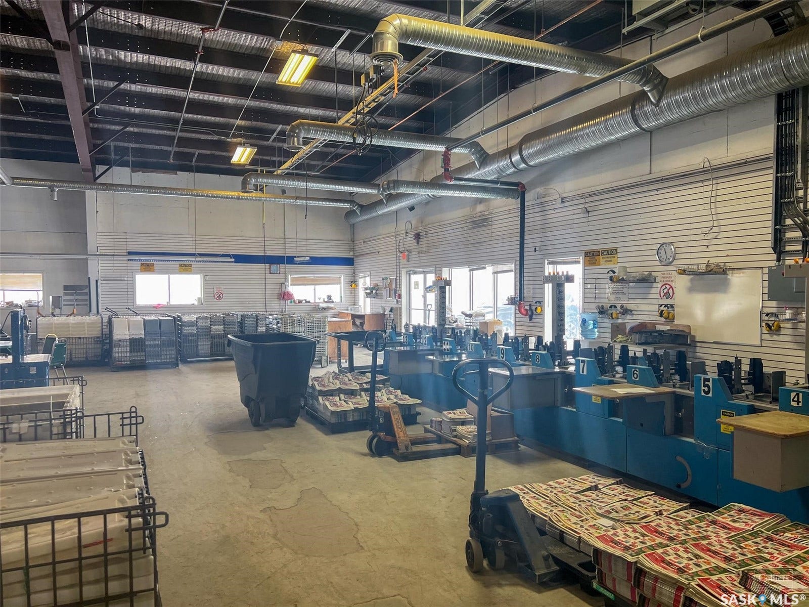 High ceilings with exposed ductwork, multiple windows providing natural light, durable concrete flooring, and overhead lighting fixtures