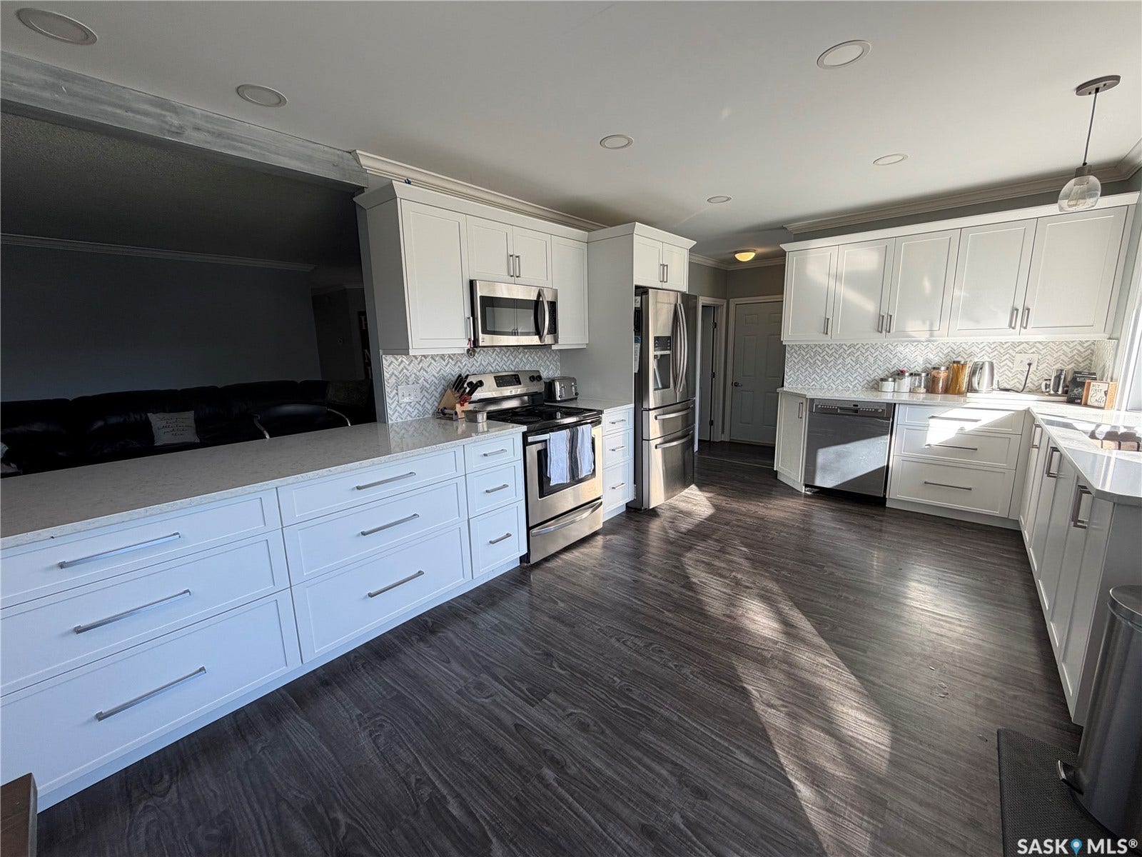White shaker cabinetry, stainless steel appliances, light-toned countertops, wood-finish flooring, and a patterned backsplash
