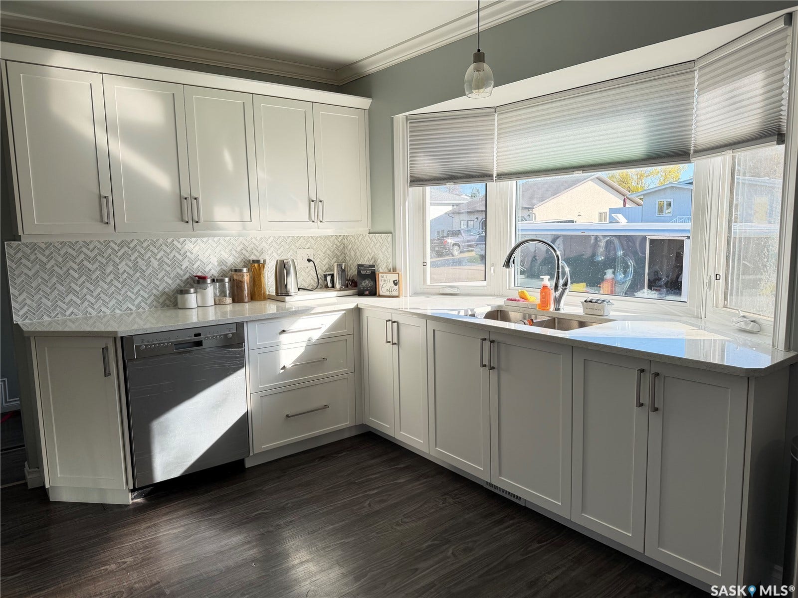White shaker cabinetry with crown molding, chevron tile backsplash, light-colored countertops, stainless steel sink with a gooseneck faucet, and dark wood-finish flooring