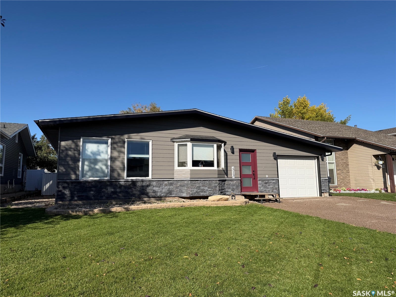 Contemporary exterior with gray siding, a red entry door, a white garage door, a bay window, and a manicured lawn