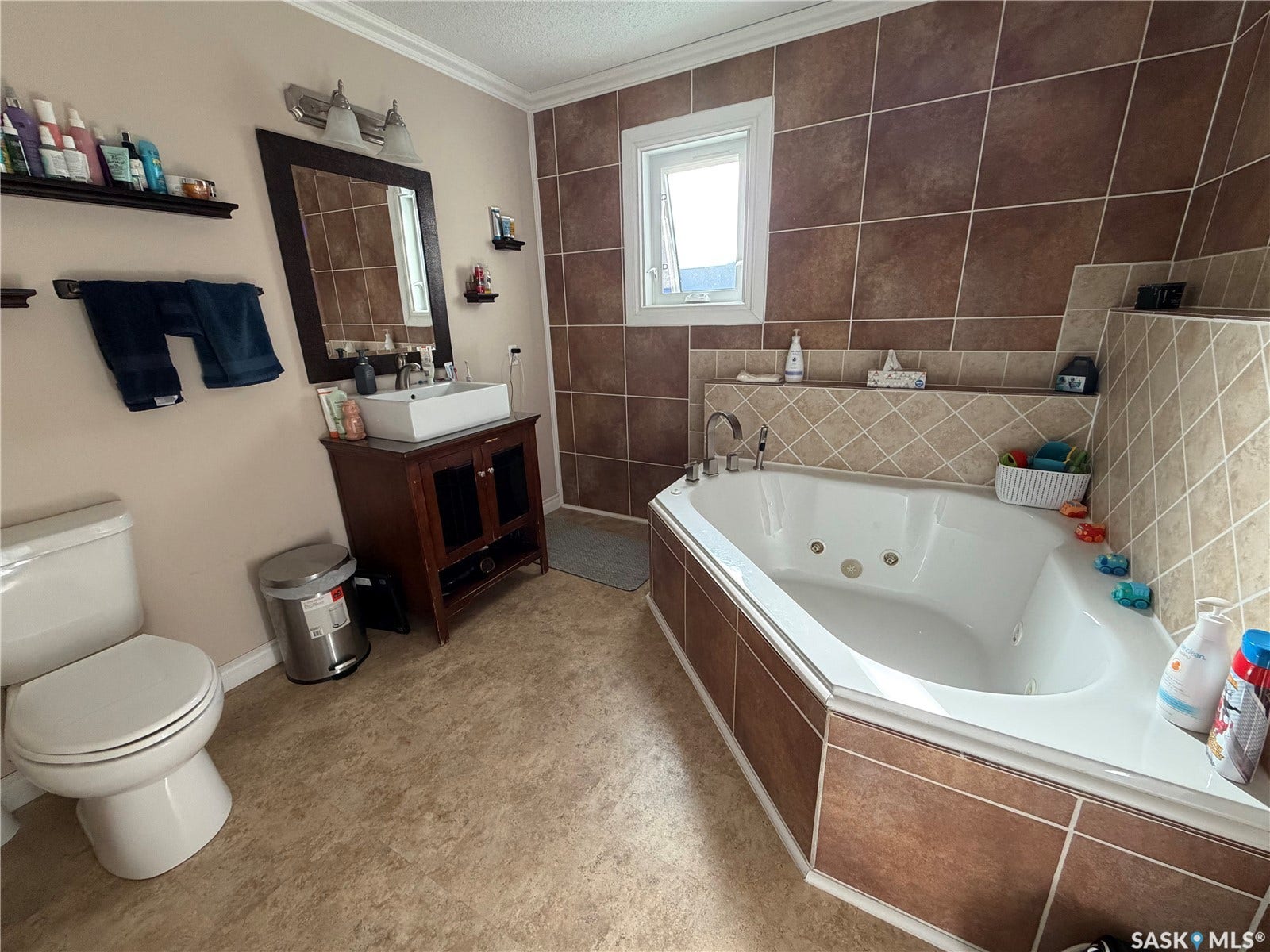 Spacious bathroom featuring a built-in jetted tub, ceramic tile surround, and a vanity with a vessel sink