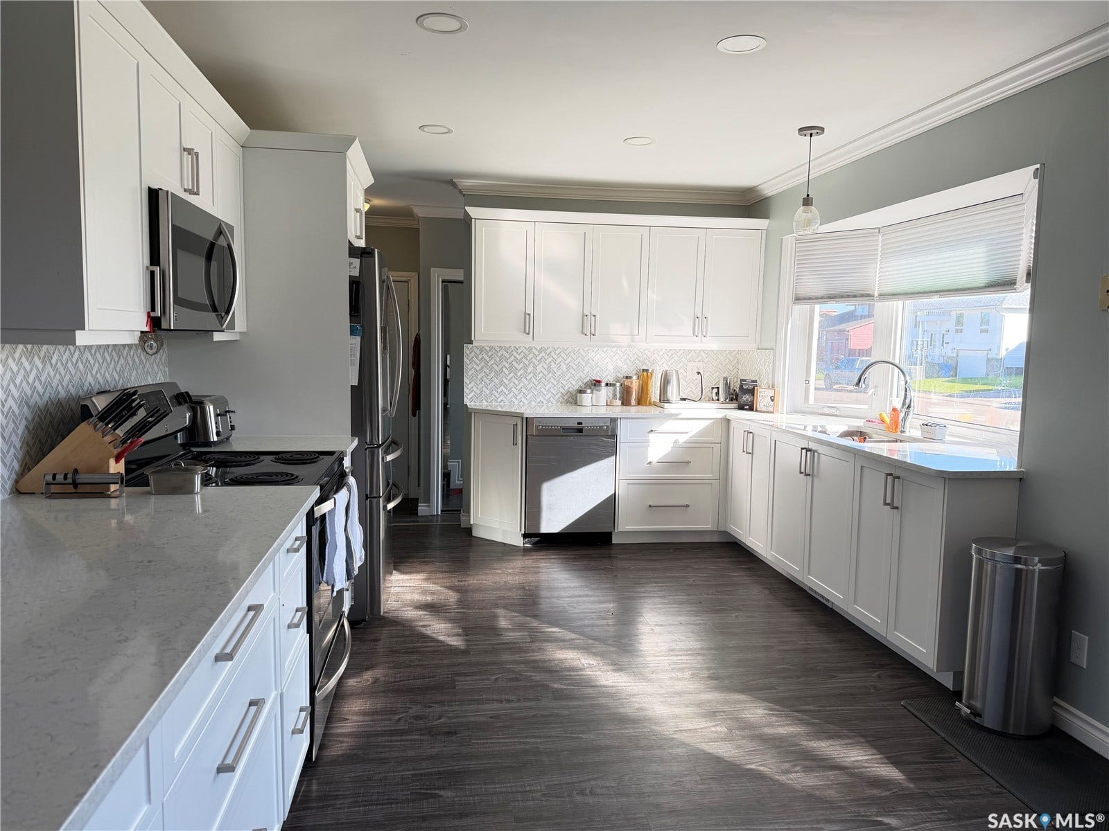U-shaped kitchen with white cabinetry, stainless steel appliances, herringbone tile backsplash, and dark wood-finish flooring