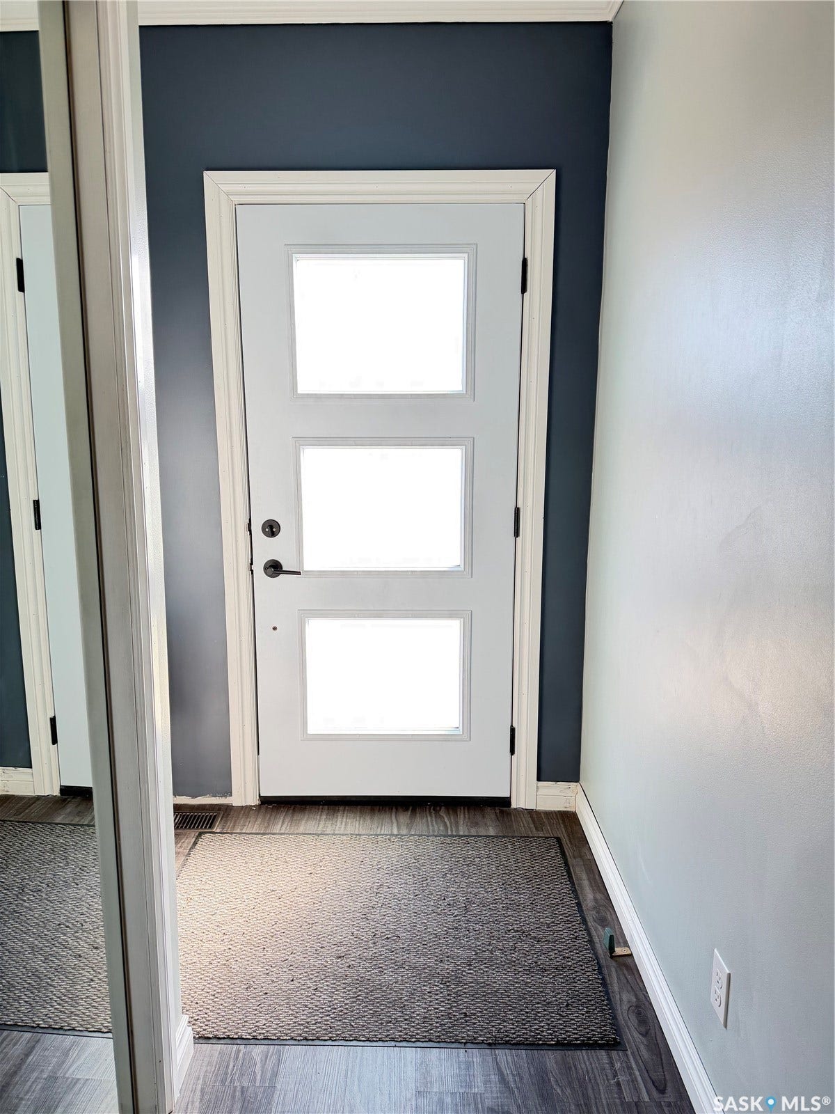 Three-panel glass door with dark hardware, dark accent wall, white trim throughout, and wood-finish flooring