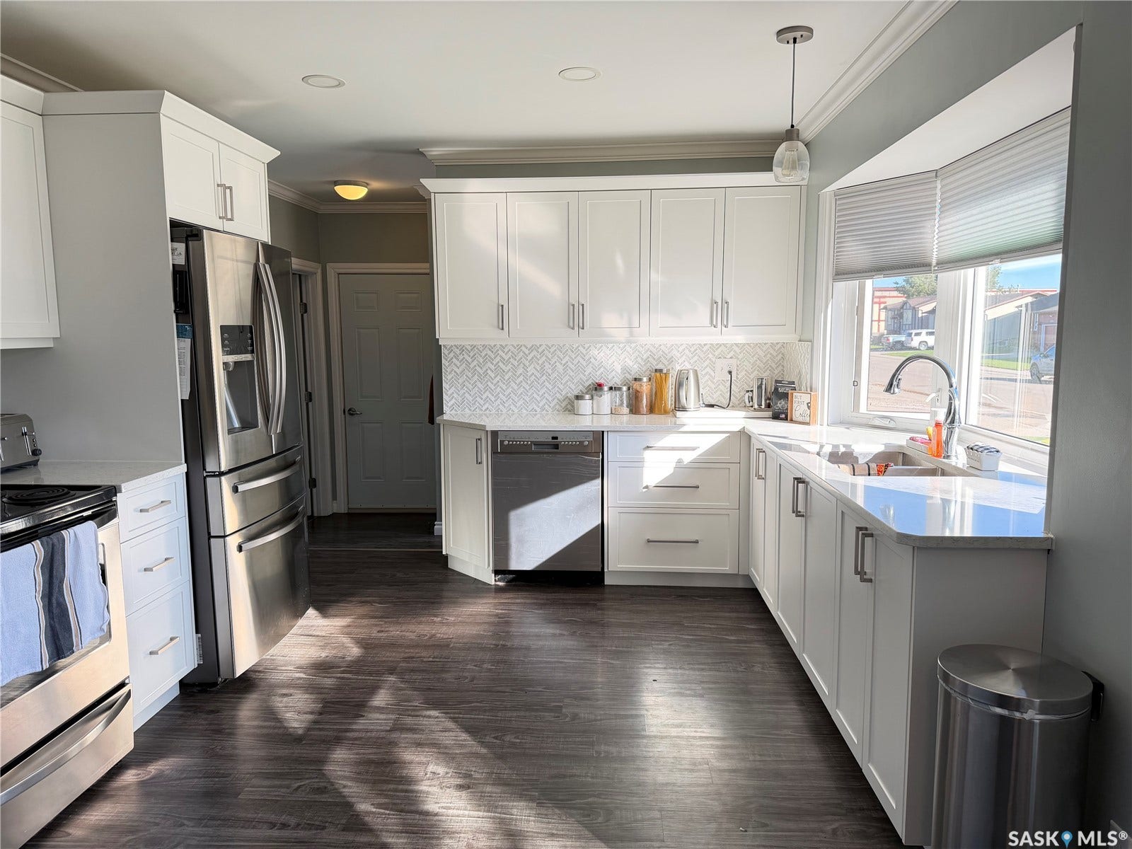 Modern kitchen with white cabinetry, stainless steel appliances, wood-finish flooring, white countertop, and a tiled backsplash