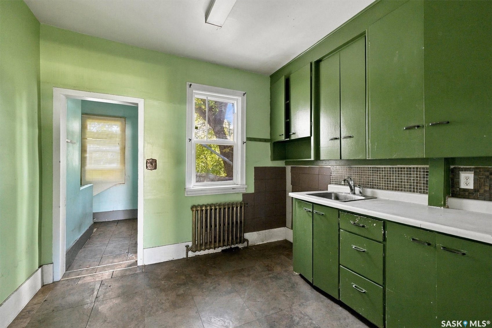 Kitchen featuring wall-mounted cabinetry, white countertops, stainless steel sink, and tiled backsplash