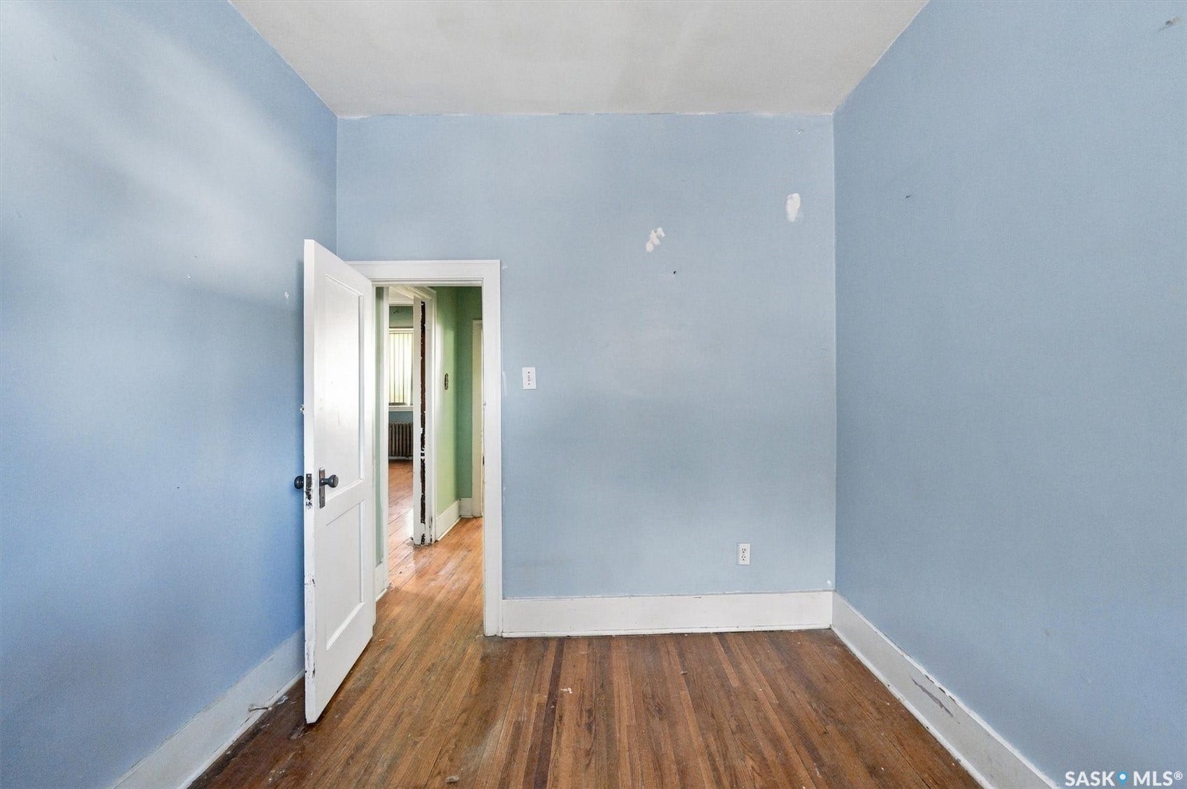 Wood-finish flooring with white trim, a painted interior door, and light blue walls