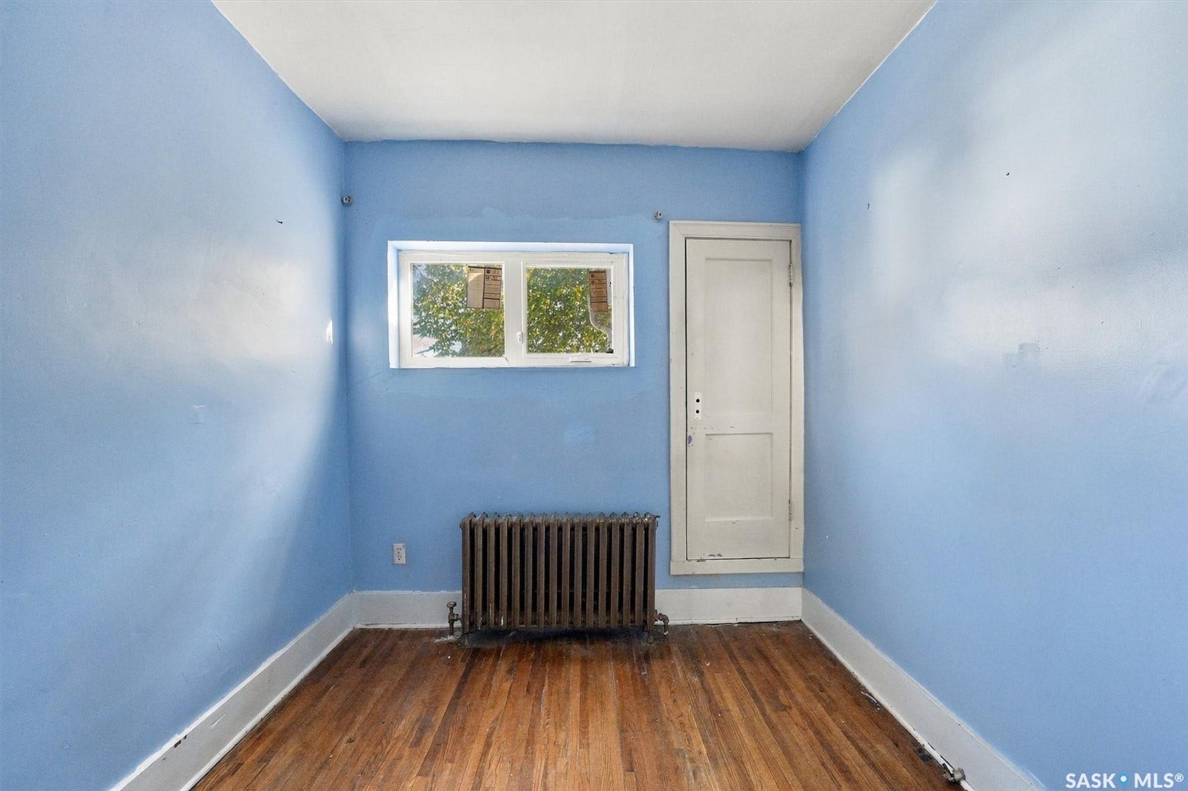 Hardwood flooring, white trim, rectangular window, built-in storage, and a cast-iron radiator