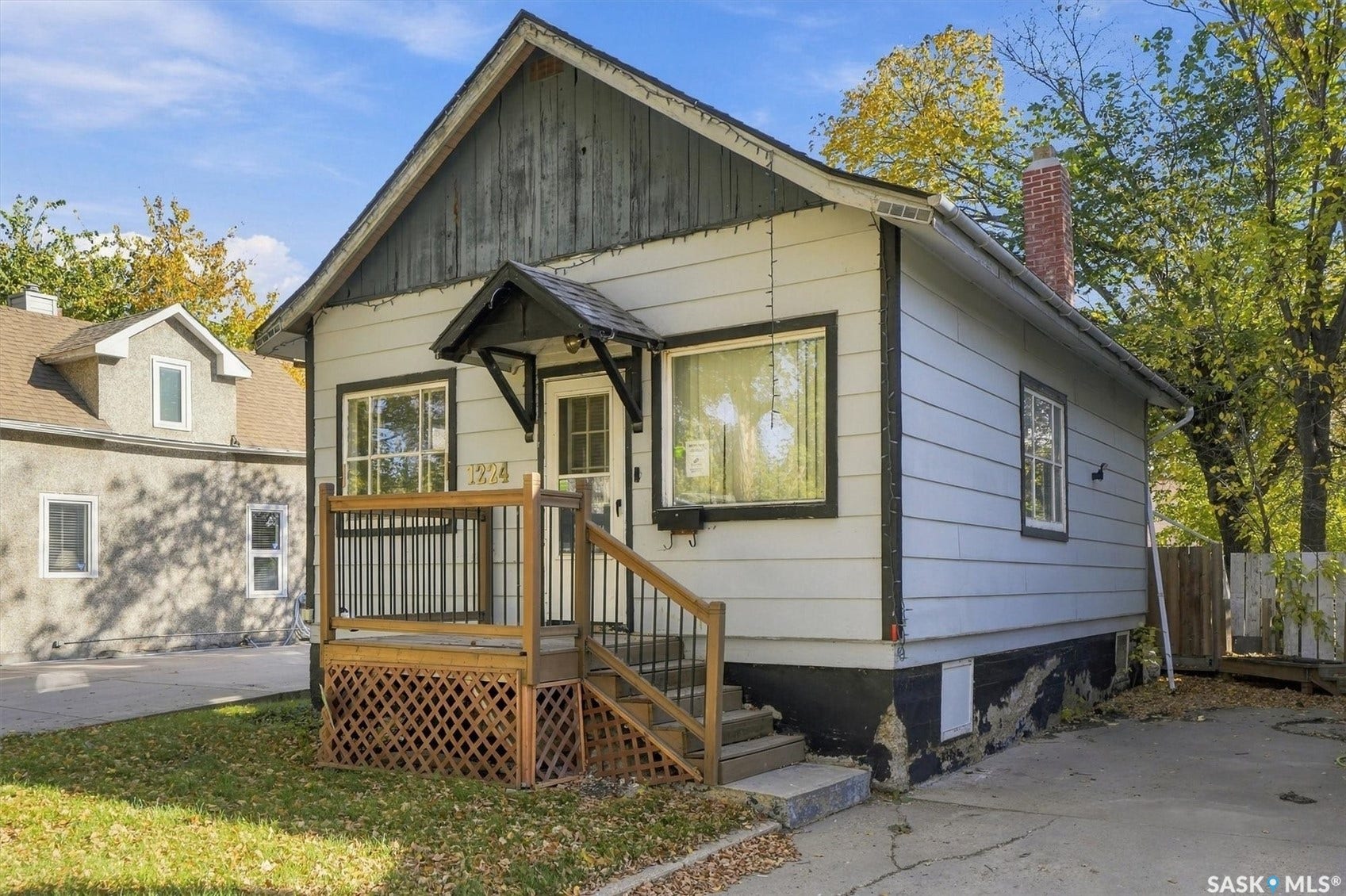 Light-colored siding exterior, dark trim accents, brick chimney, front porch with wood railings and lattice detailing, asphalt driveway