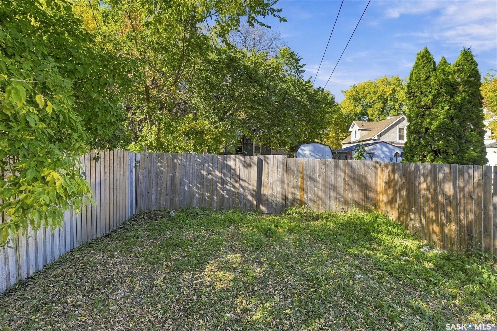 Fenced yard with mixed-panel fencing, featuring a partial grass lawn and mature trees