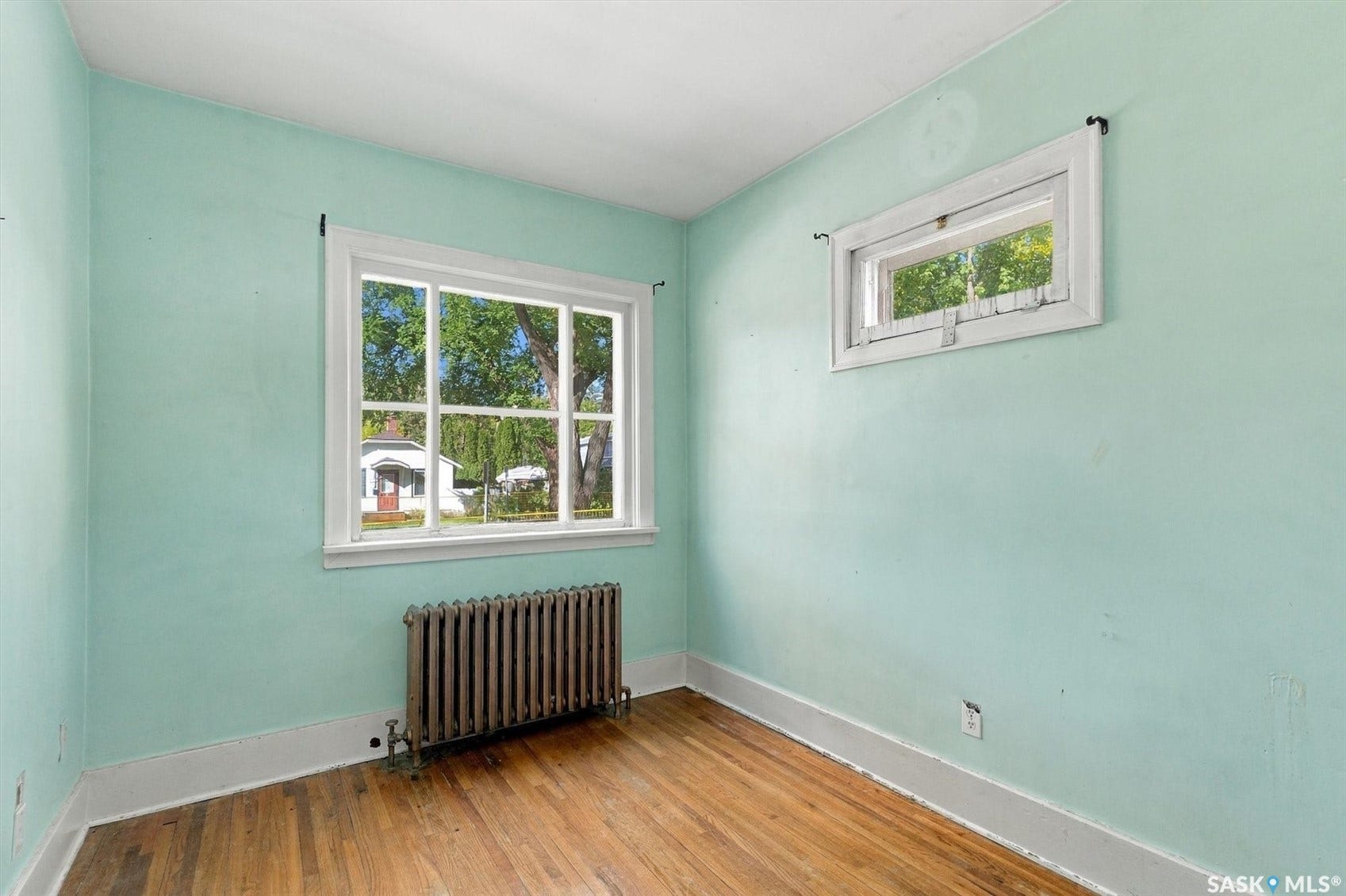 Hardwood flooring, two windows with white trim, and a radiator unit