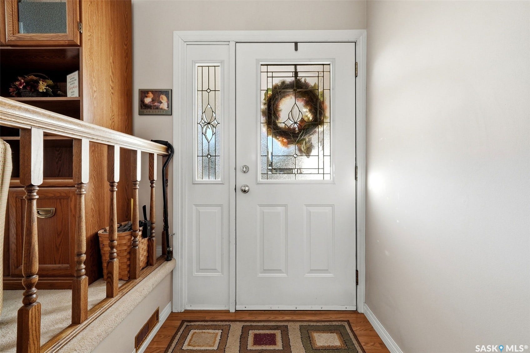White entry door with decorative glass, coordinating sidelight, and wood-finish flooring